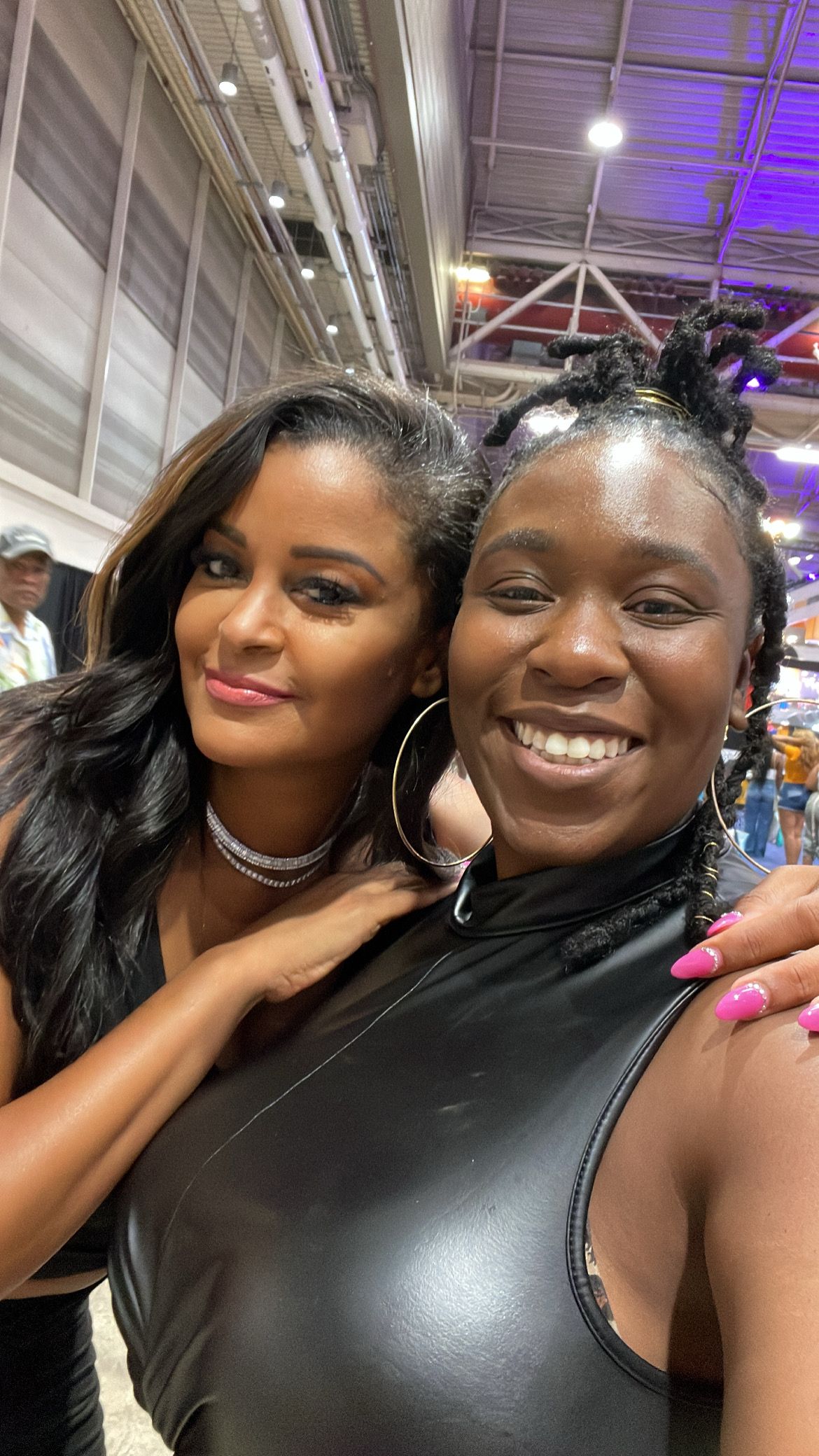 Two friends in black outfits pose together at an indoor event.