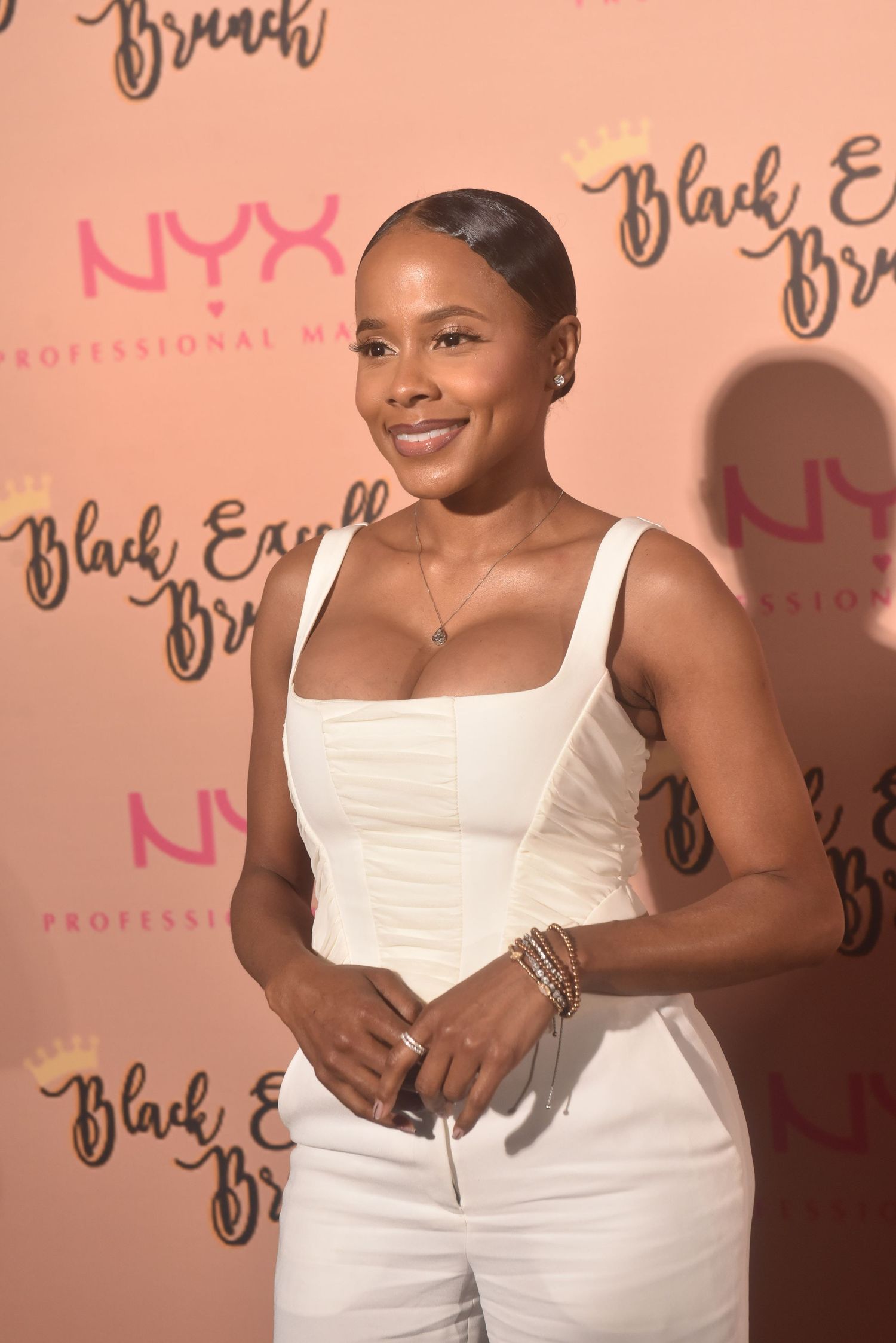 Woman in white outfit smiling at Black Excel Brunch event sponsored by NYX Professional Makeup.