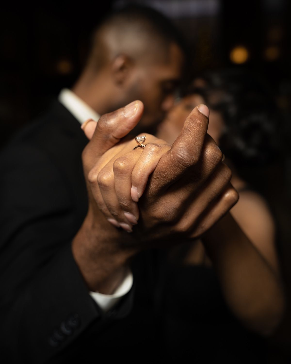 Close-up of hands clasped together showing an engagement ring in elegant formal wear.