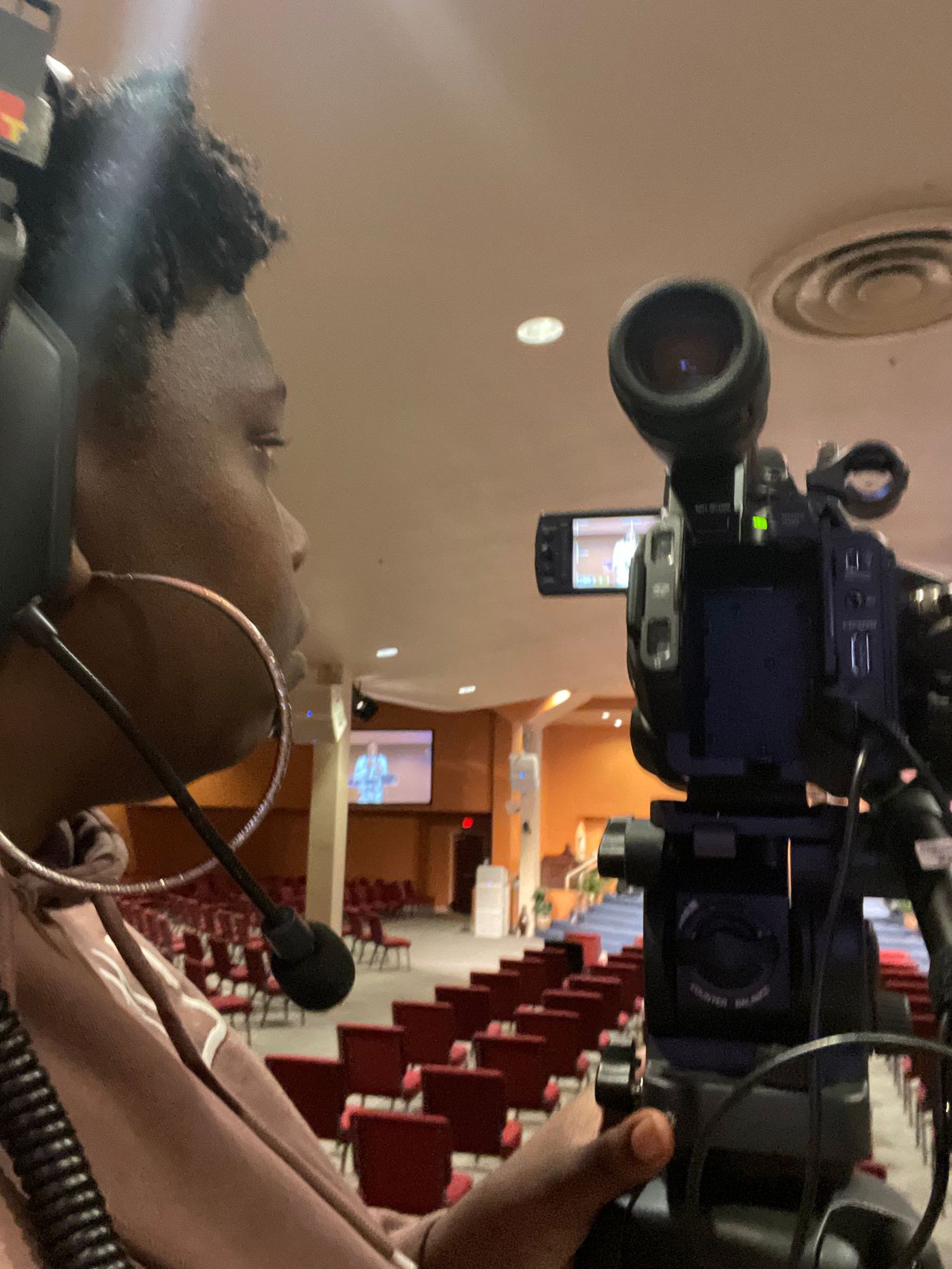 A camera operator working with professional video equipment in an auditorium setting.