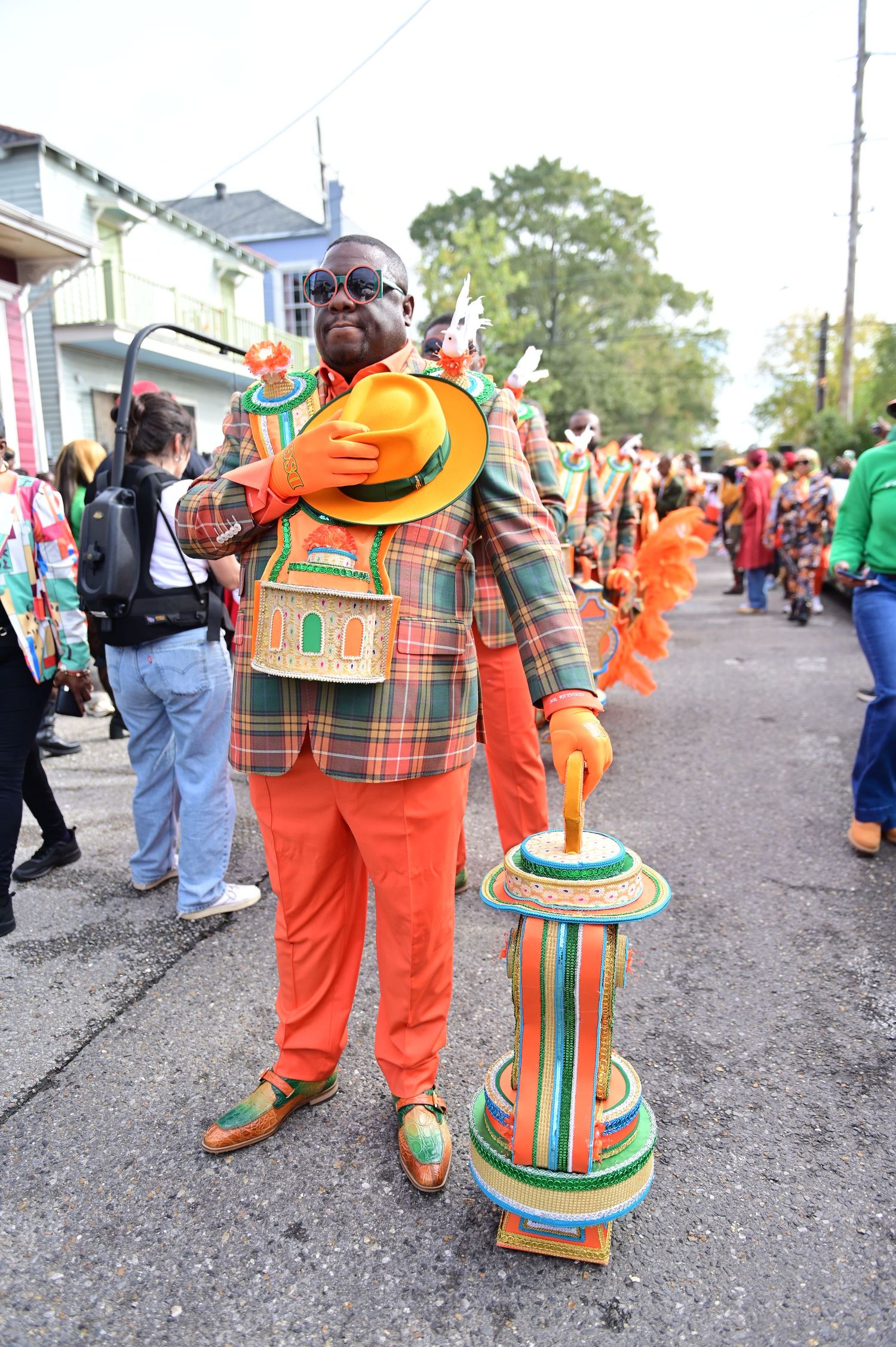 People in bright orange costumes with decorative plaid patterns at a street parade or festival.