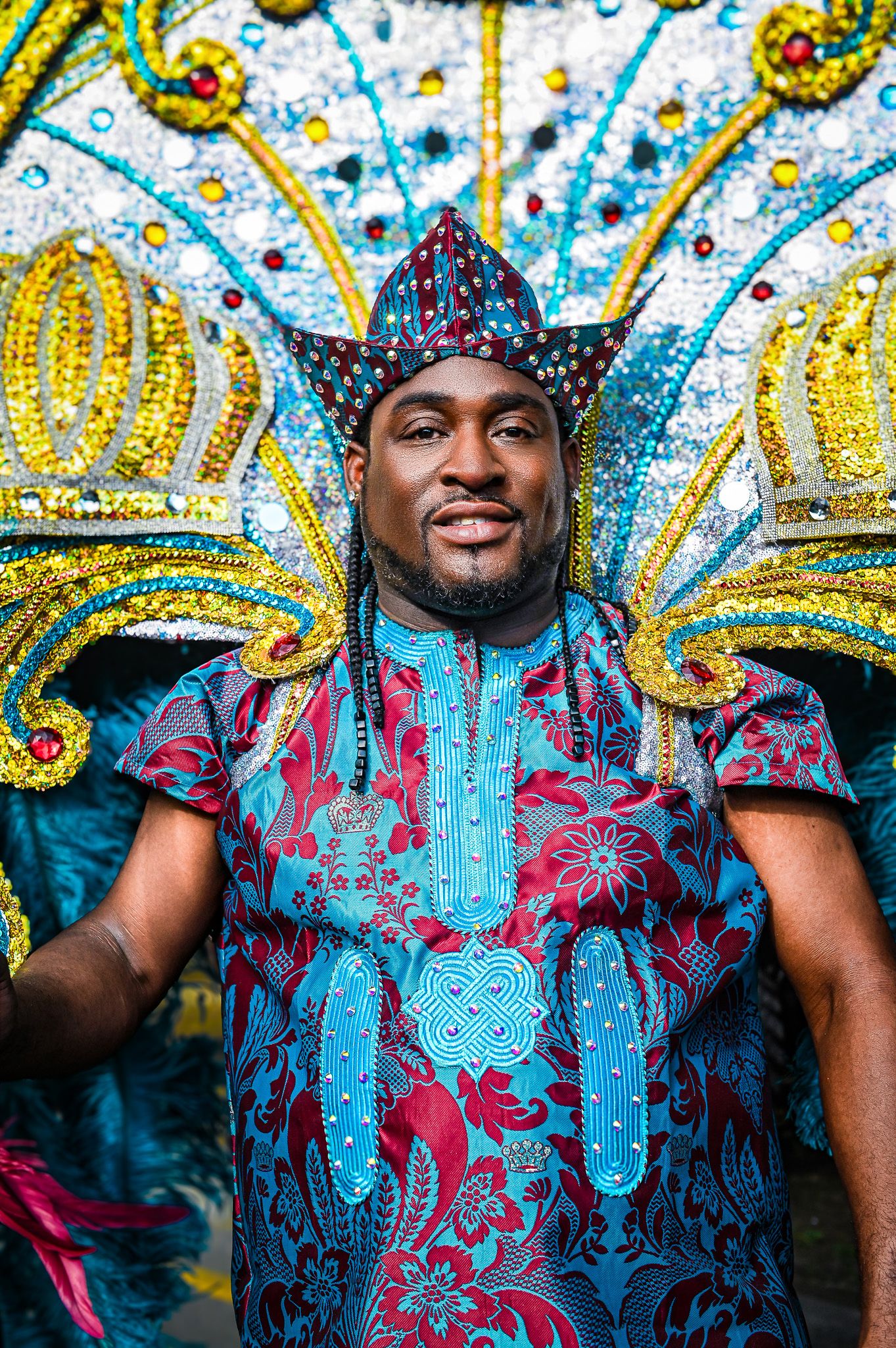 Person wearing colorful African print outfit poses against vibrant patterned backdrop.