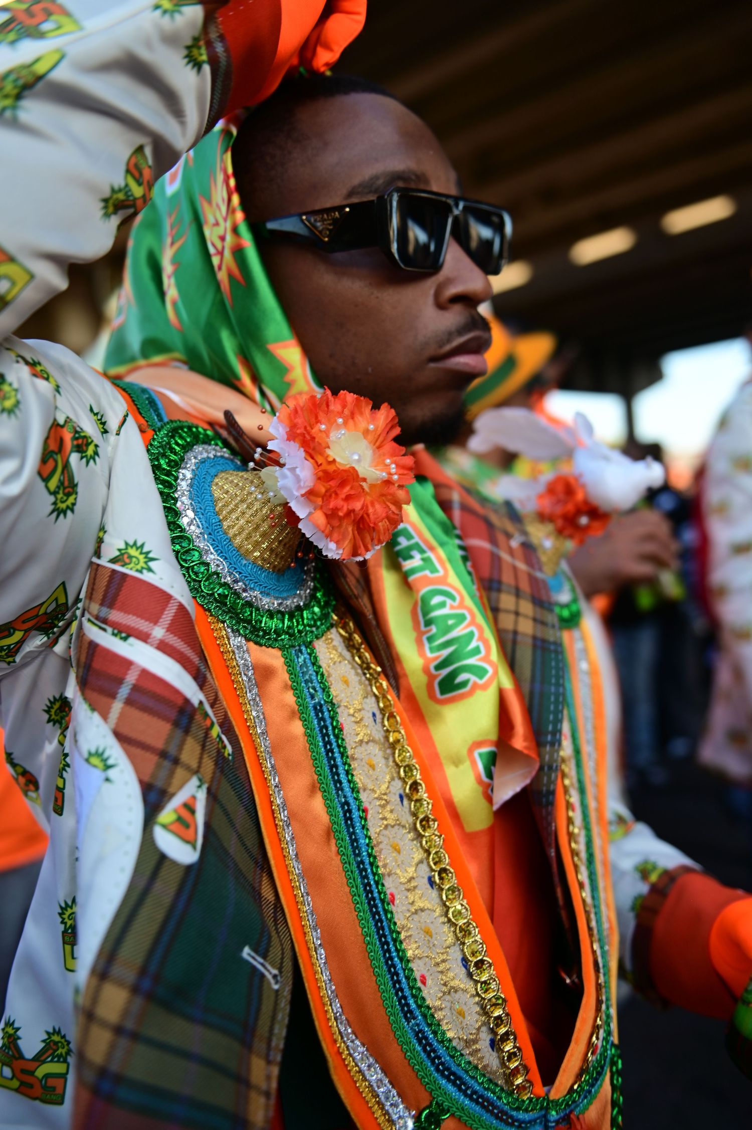 Festival participant wearing sunglasses and ornate costume with orange and green decorative elements.