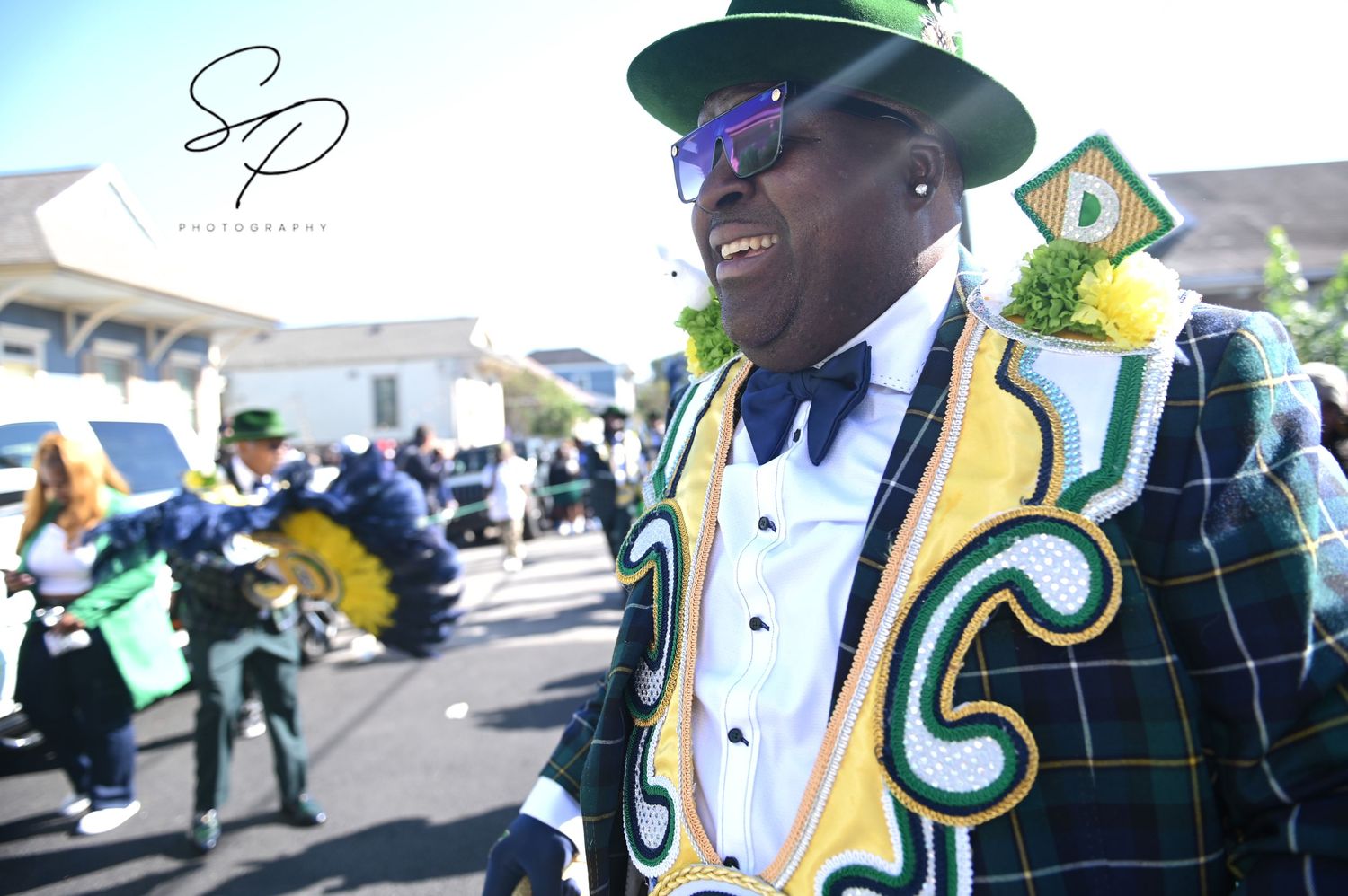 Performers in plaid uniforms and green feathered hats marching in a parade.