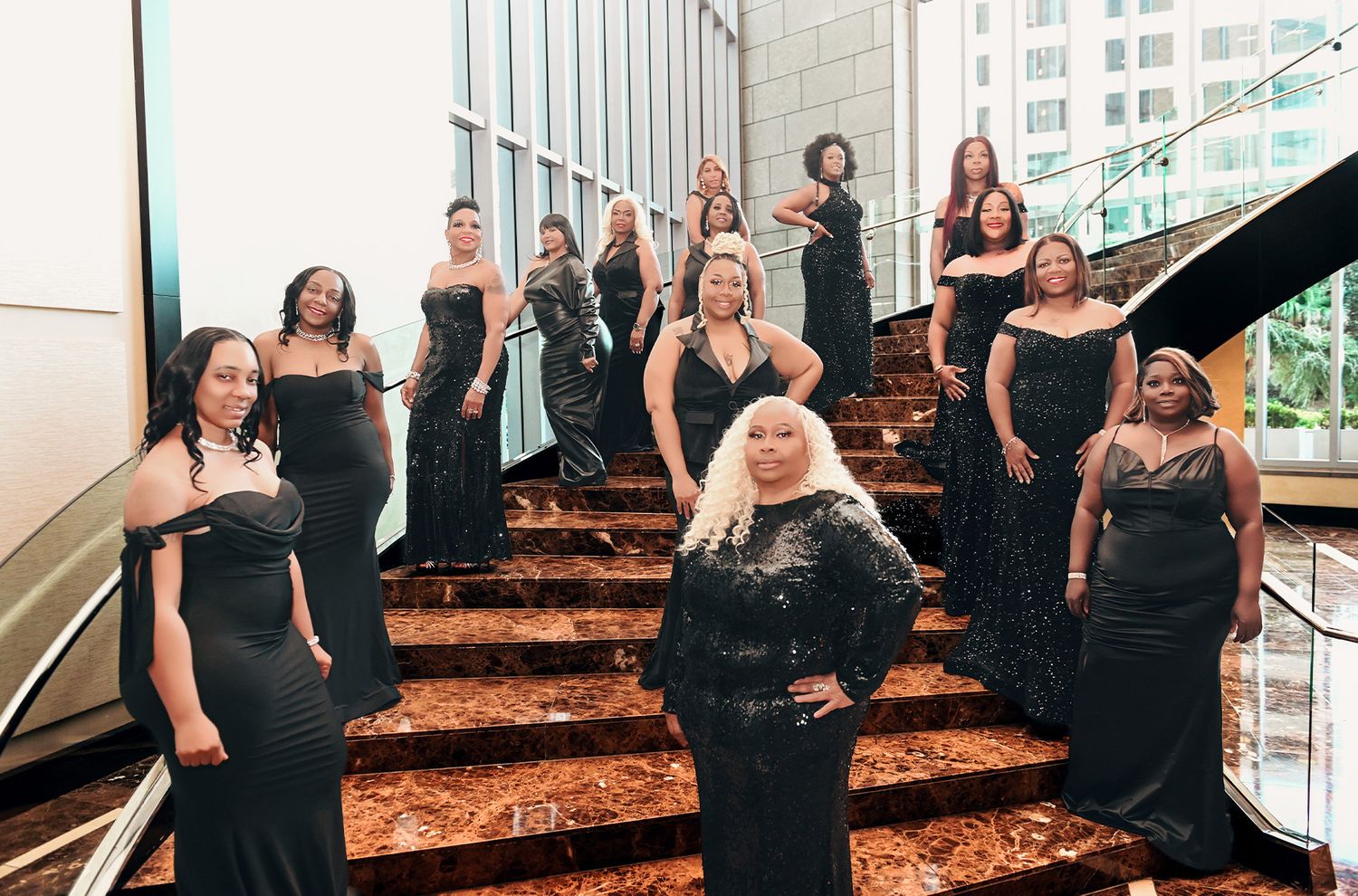 Group wearing black dresses poses on elegant marble staircase for formal event photos.