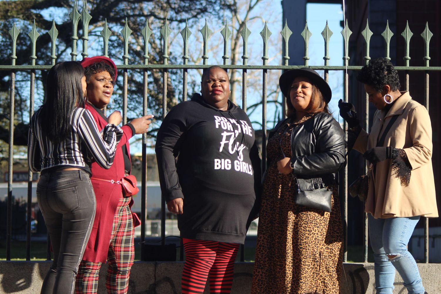 People gathered outdoors behind decorative iron fence gates during daytime event.