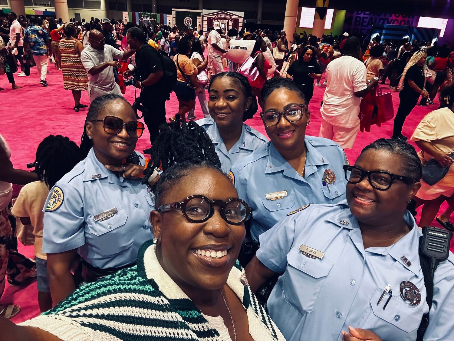 Group photo of uniformed staff members at a crowded event with pink lighting.