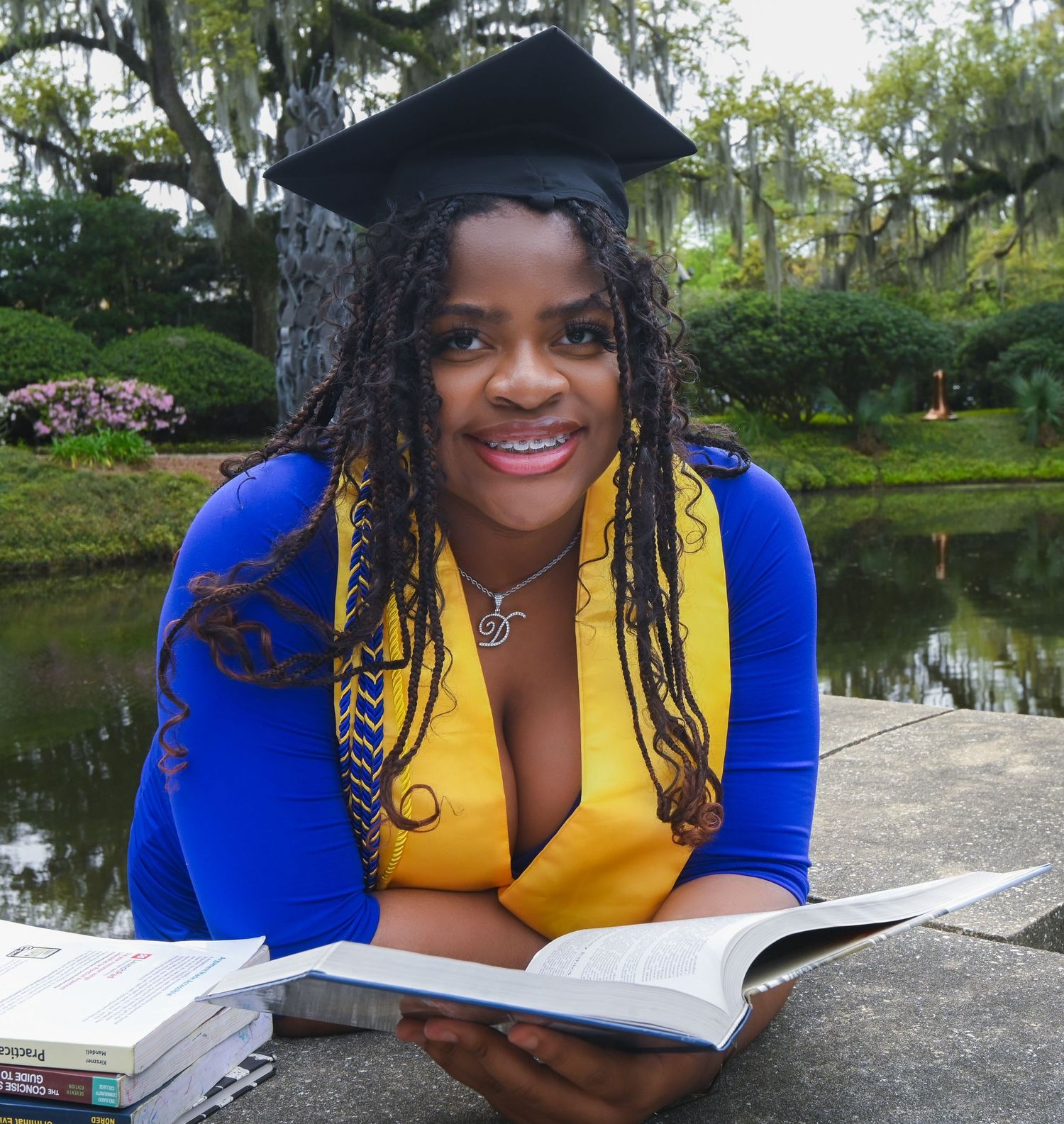 Student reading outdoors in bright blue and yellow attire by a serene pond.