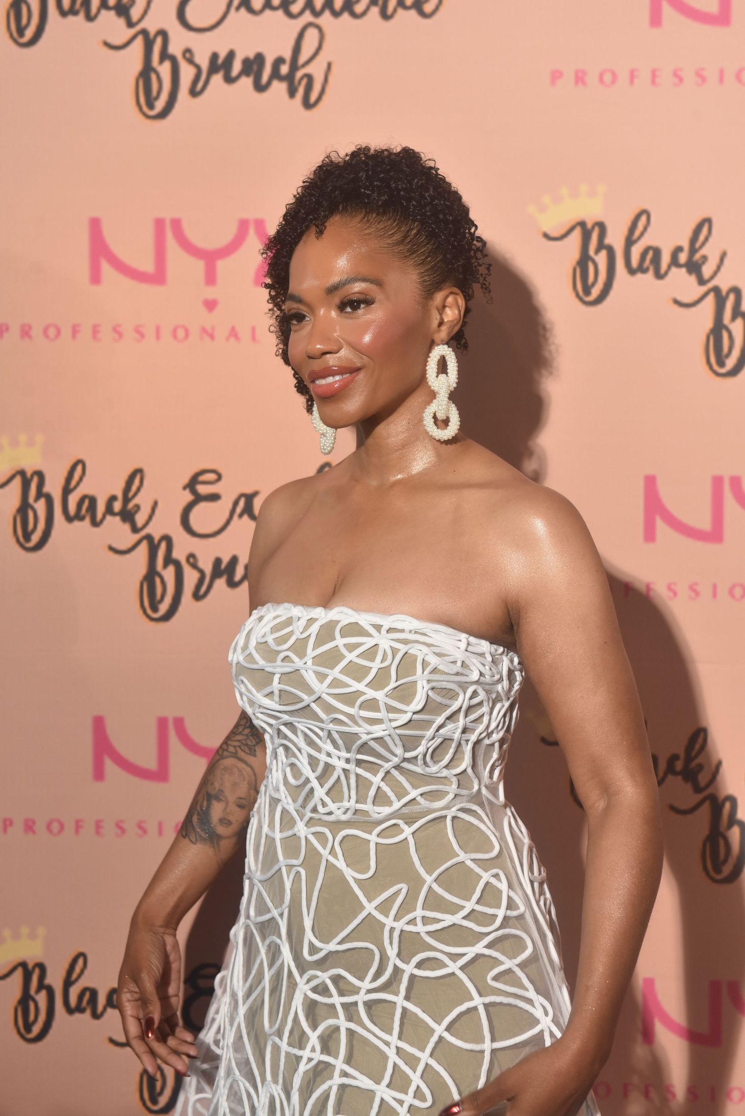 Woman in white sculptural strapless dress poses at NYX Professional Makeup Black Excellence Brunch event.