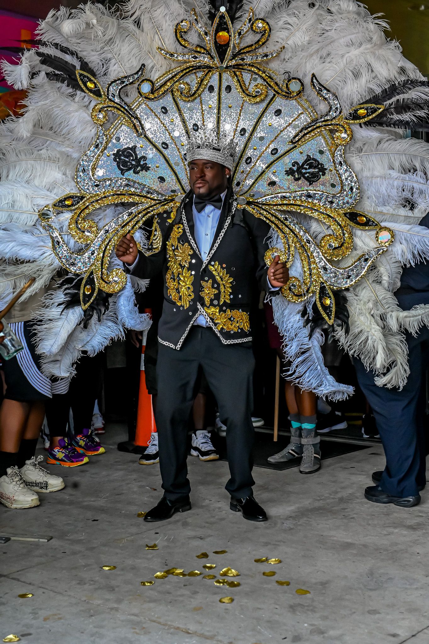 Mardi Gras performer in black suit with spectacular white feather and gold butterfly wing costume display.