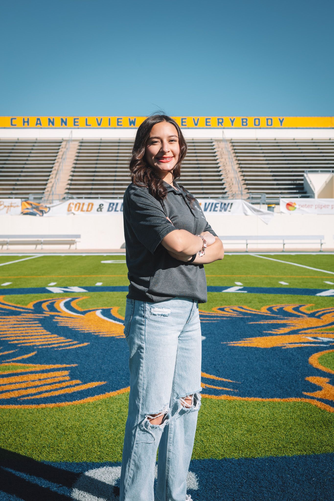 Someone stands confidently on a football field with stadium seating and 'CHANNELVIEW EVERYBODY' signage visible in background.