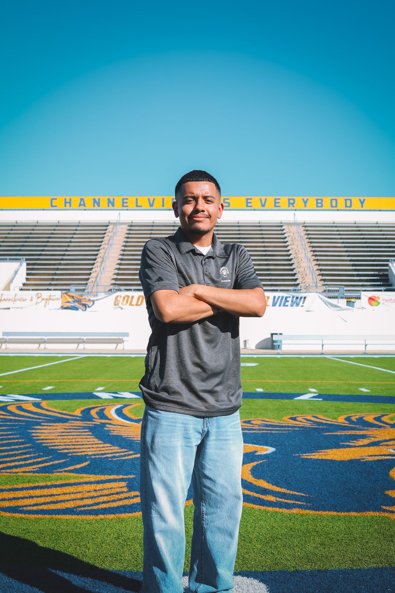 Someone stands on a football field with bright blue stadium seating and yellow signage visible in the background.