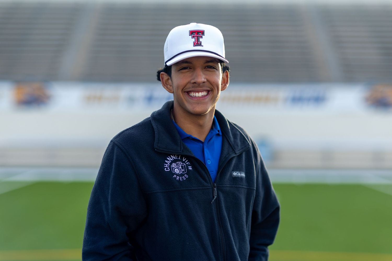 A person wearing a baseball cap and jacket poses at a sports stadium.