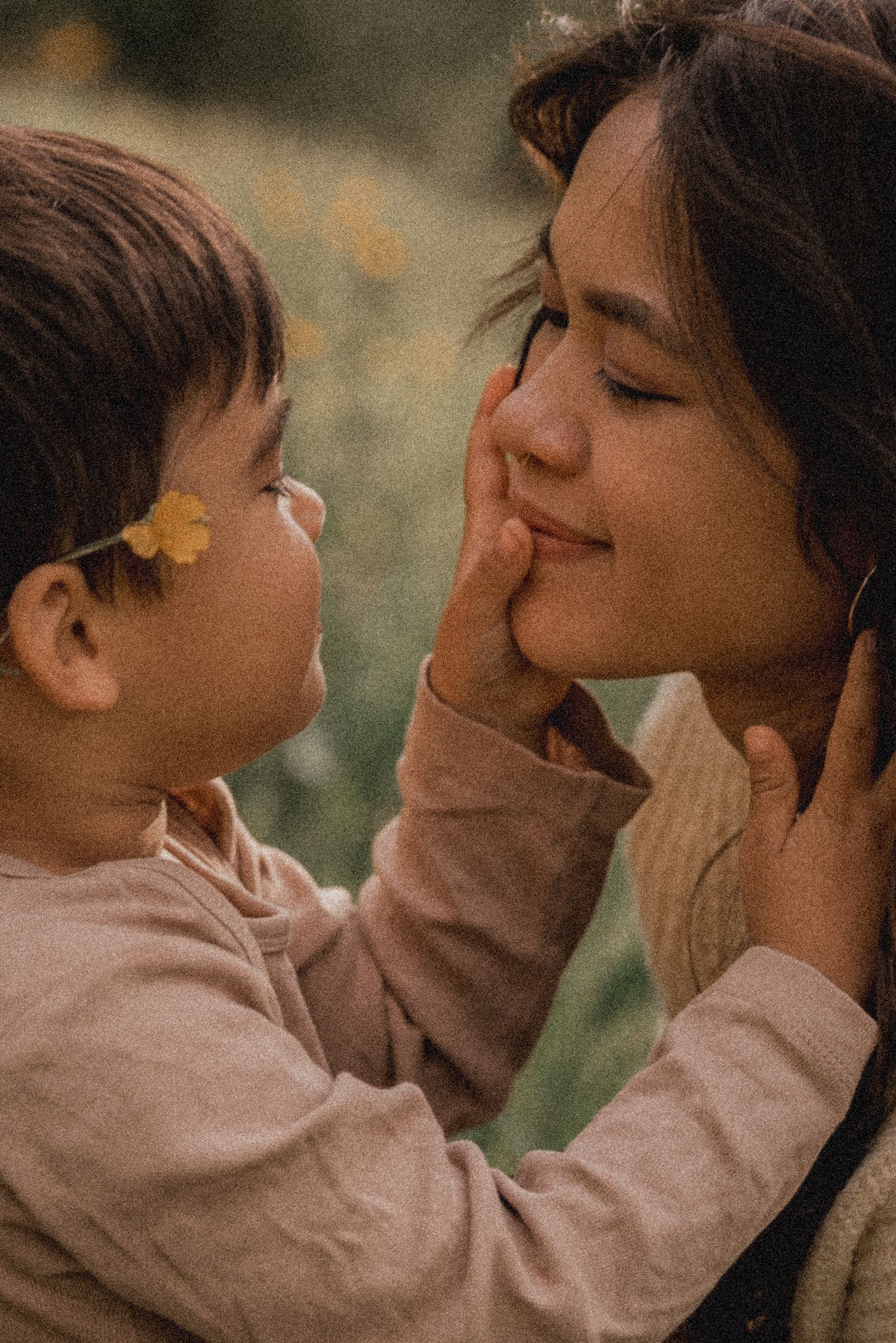 A tender moment captured between parent and child touching faces while smiling in warm lighting.