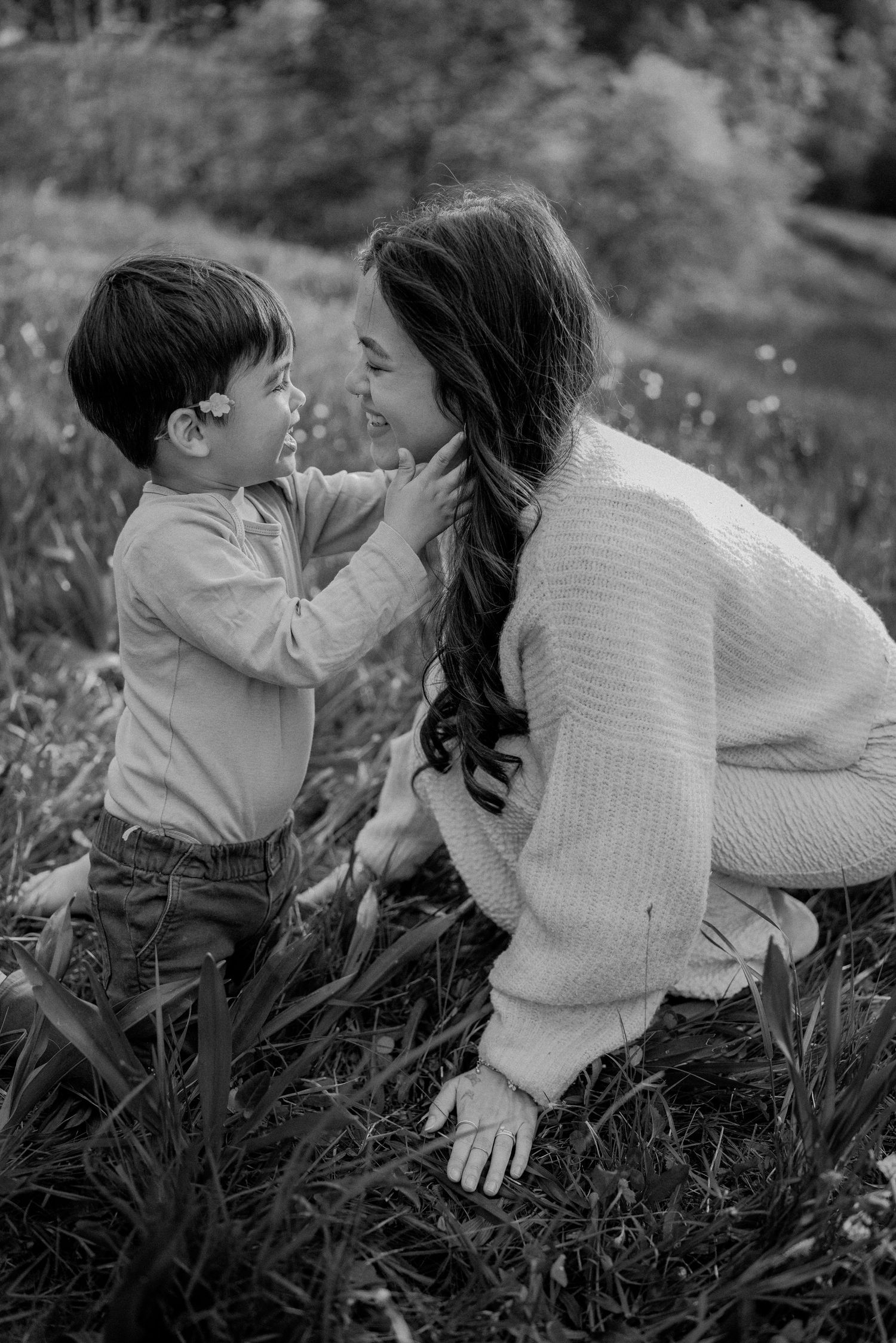An intimate black and white portrait of a parent and child sharing a tender moment in a flower-filled field.