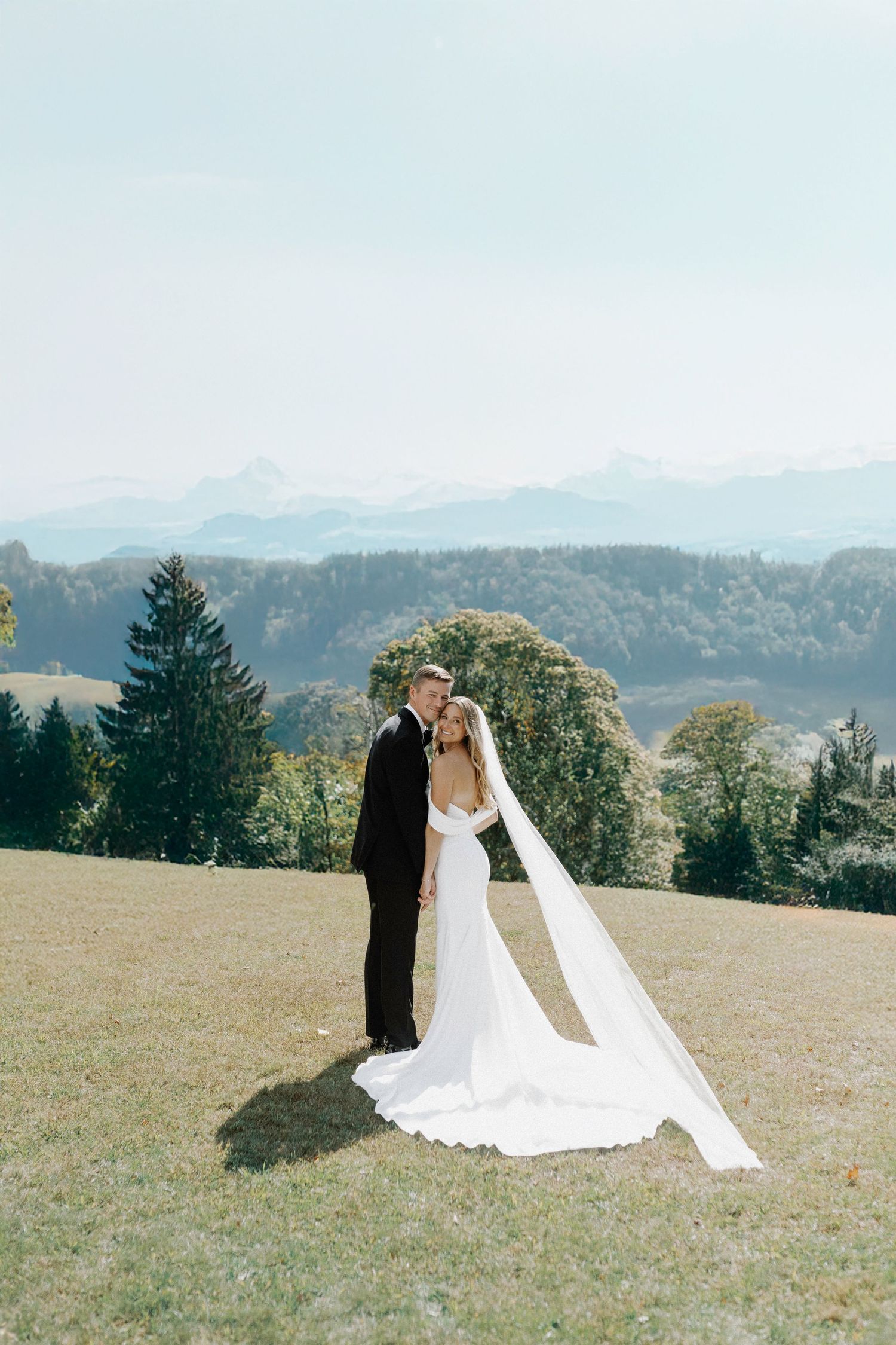 Elegant wedding couple posing on a hilltop with dramatic mountain landscape in the background.