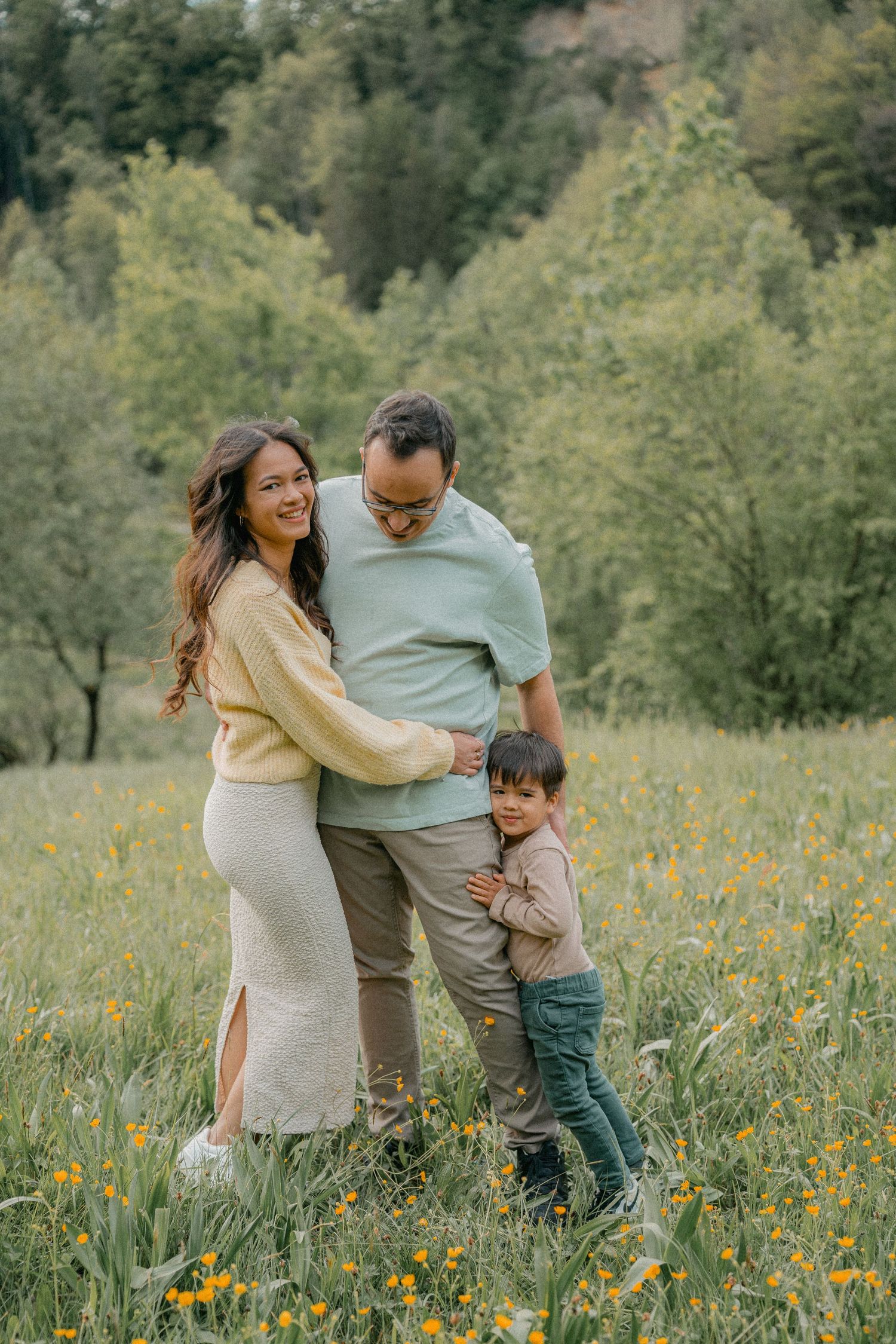 A family embraces while standing in a wildflower meadow with forested hills in the background.