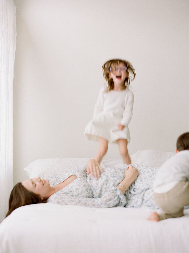 Playful family moment captured as child jumps on bed while others relax.