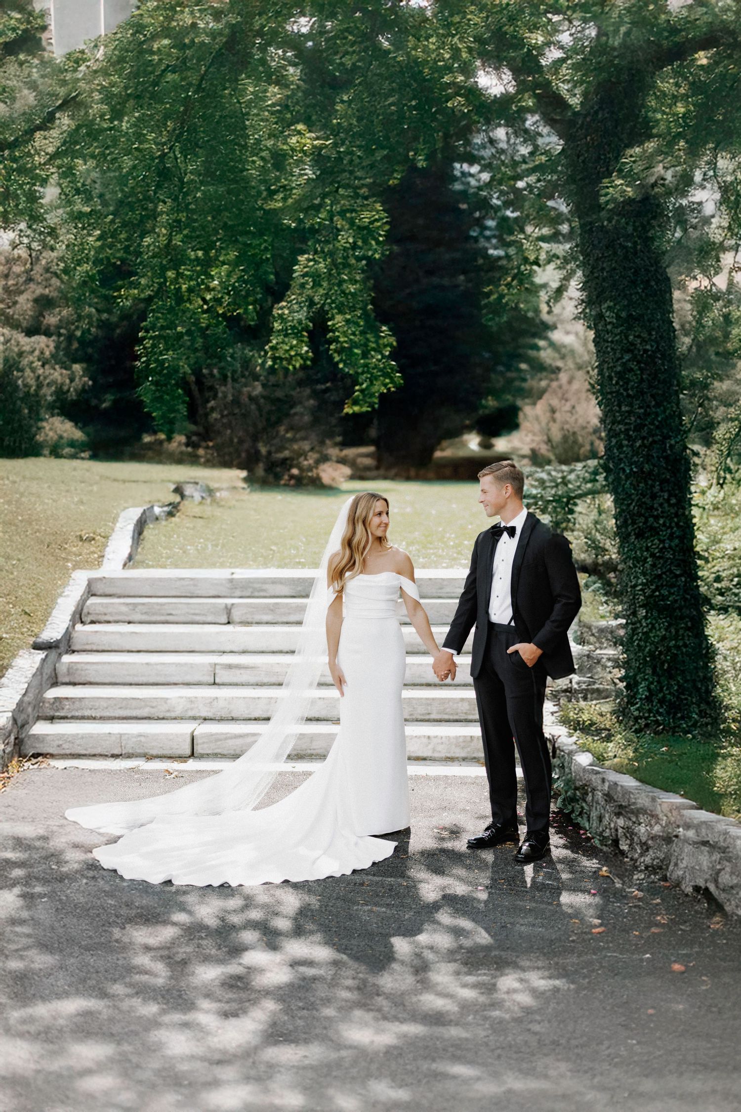 Wedding couple posing on stone steps with ivy-covered trees in the background.