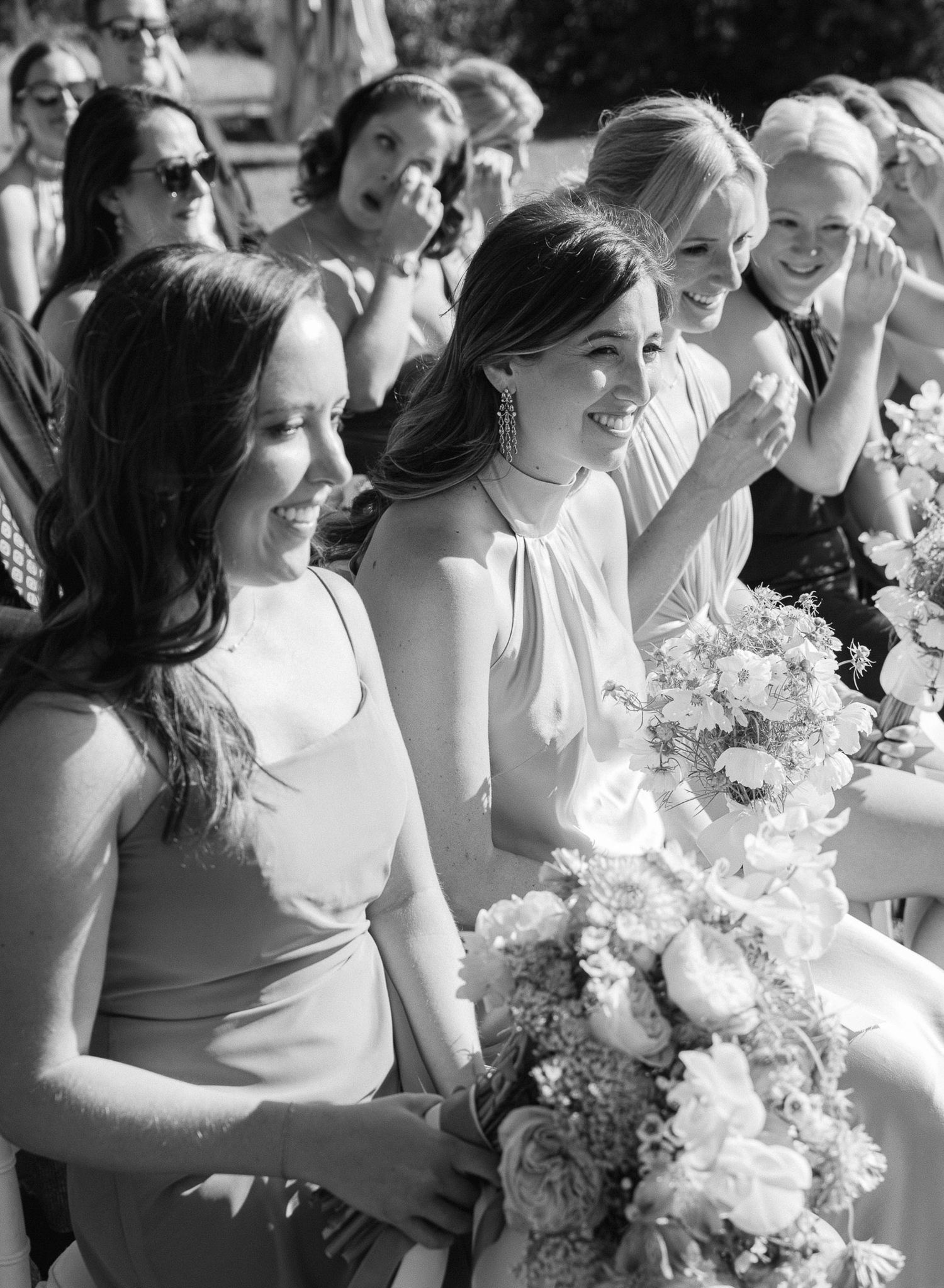 Bridesmaids in light dresses laugh and smile during outdoor wedding celebration.