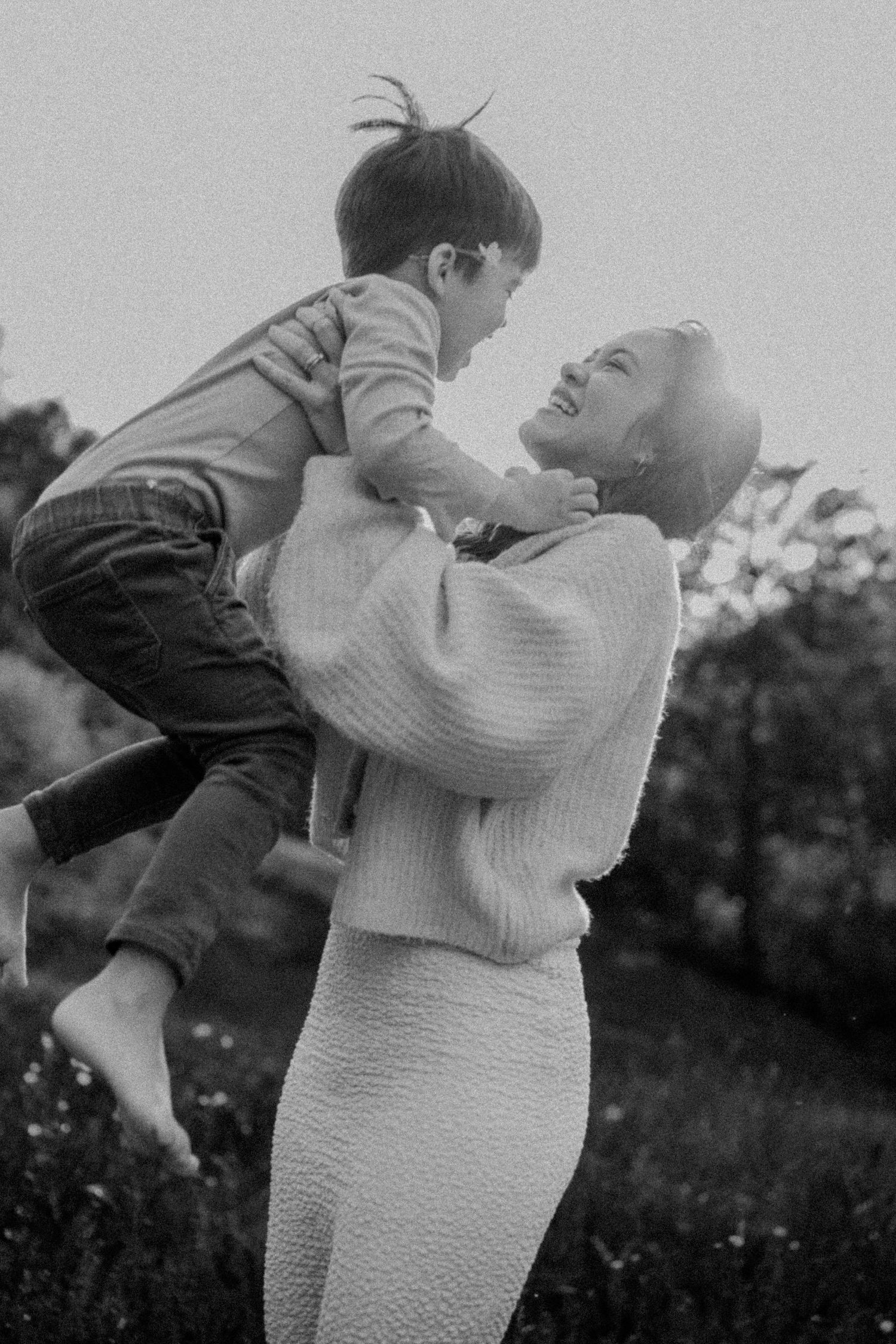 A heartwarming black and white image of a parent lifting a small child in the air outdoors.