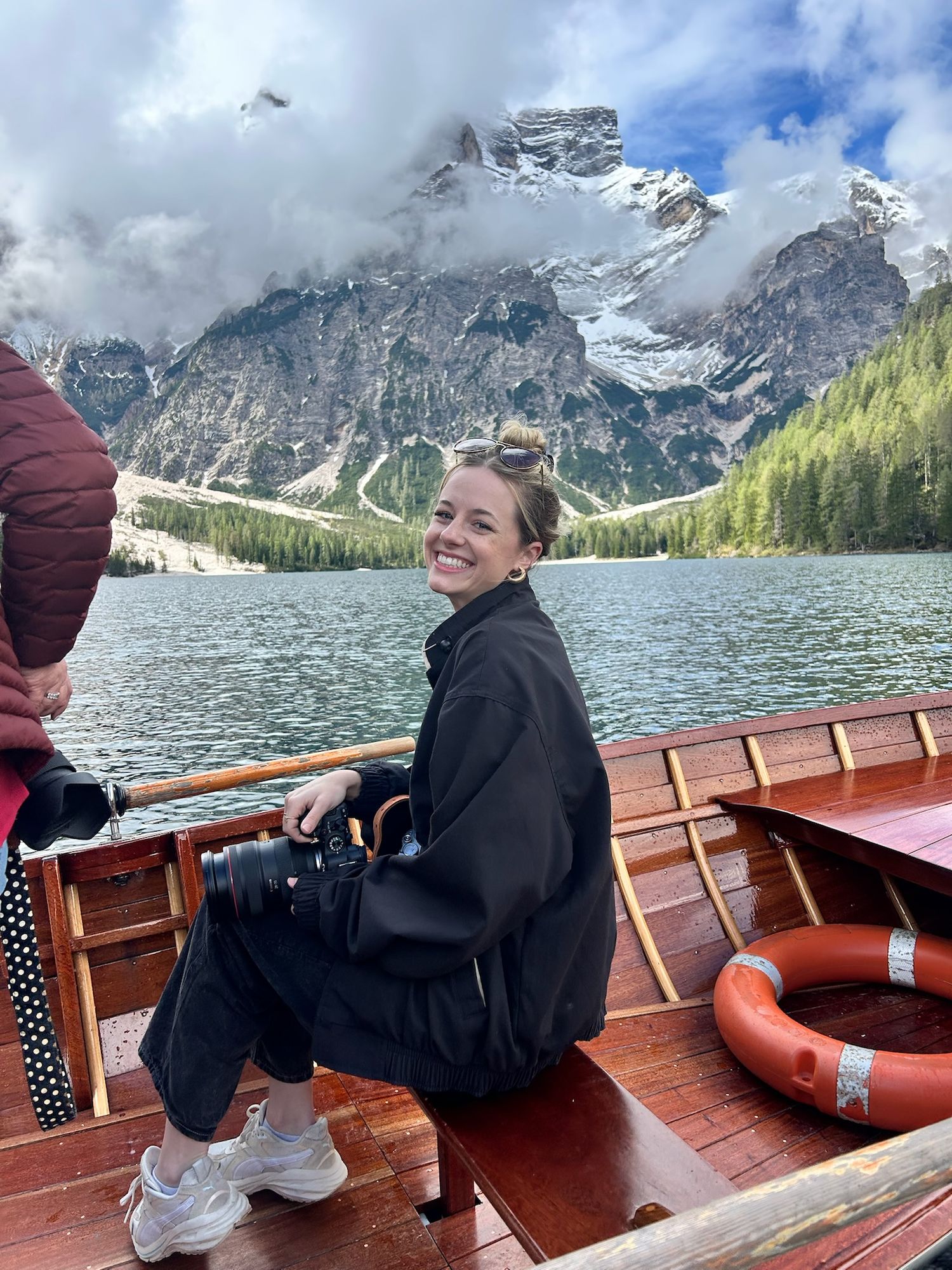 A person in a black jacket enjoys a boat ride on a scenic mountain lake with dramatic snow-capped peaks in the background.
