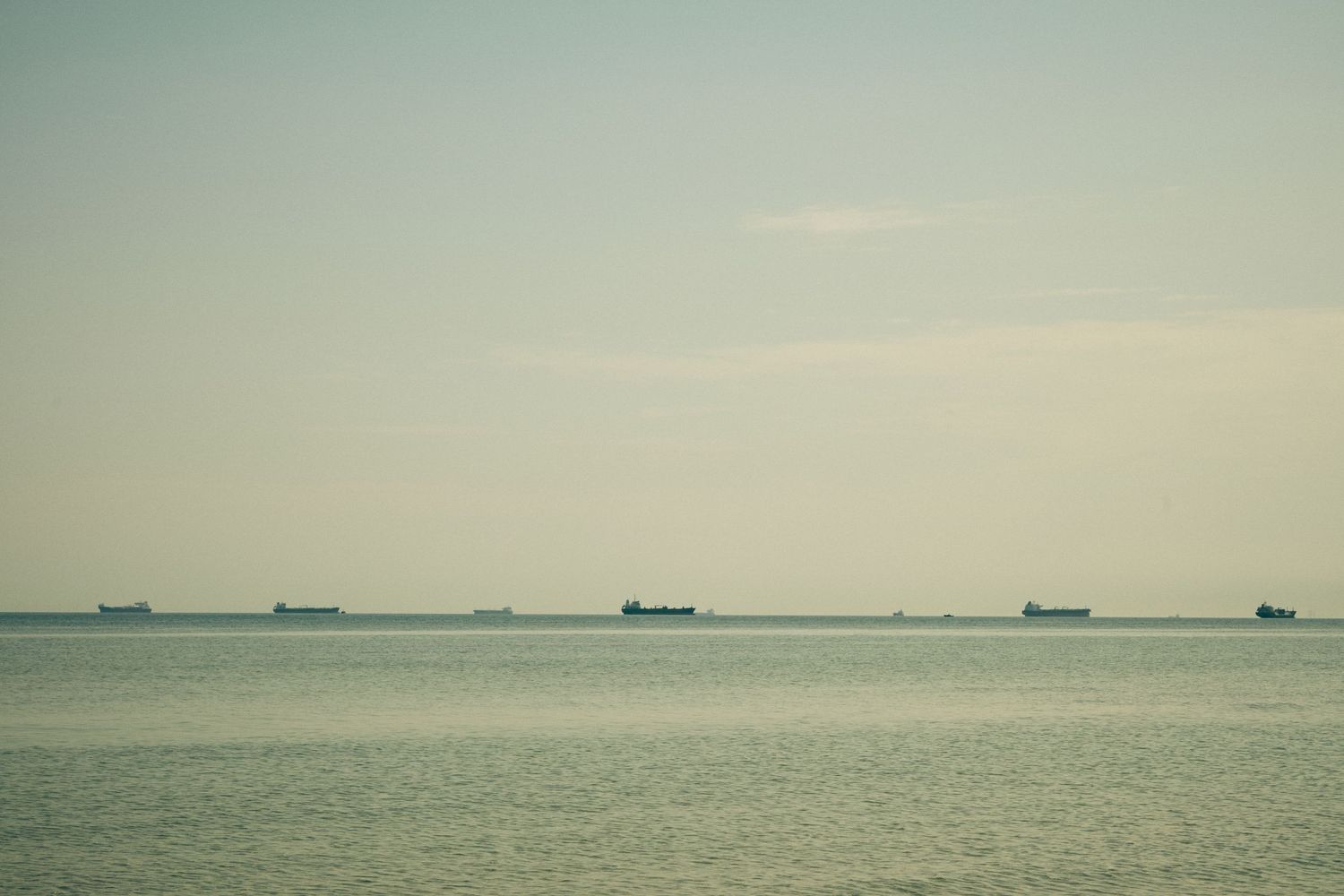 Cargo ships dot the horizon line where misty sea meets pale sky.