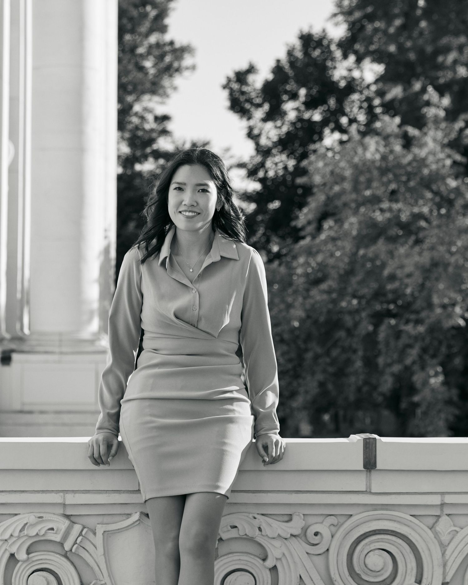 Black and white portrait of woman in fitted dress sitting on ornate architectural detail.