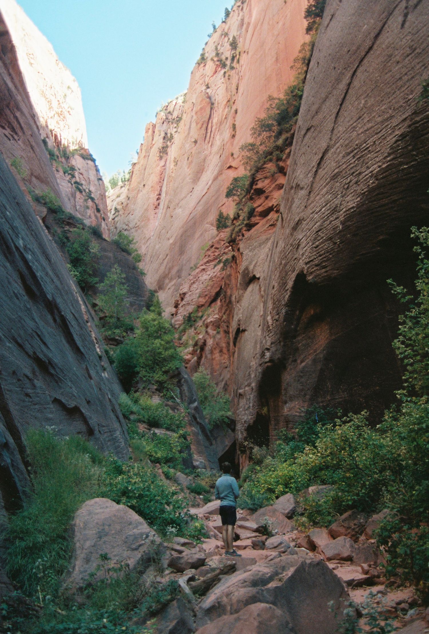 Hiker explores narrow canyon trail surrounded by towering red sandstone walls.