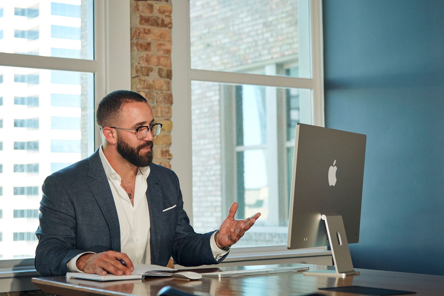 Professional gestures during work at modern desk with iMac display and exposed brick background.