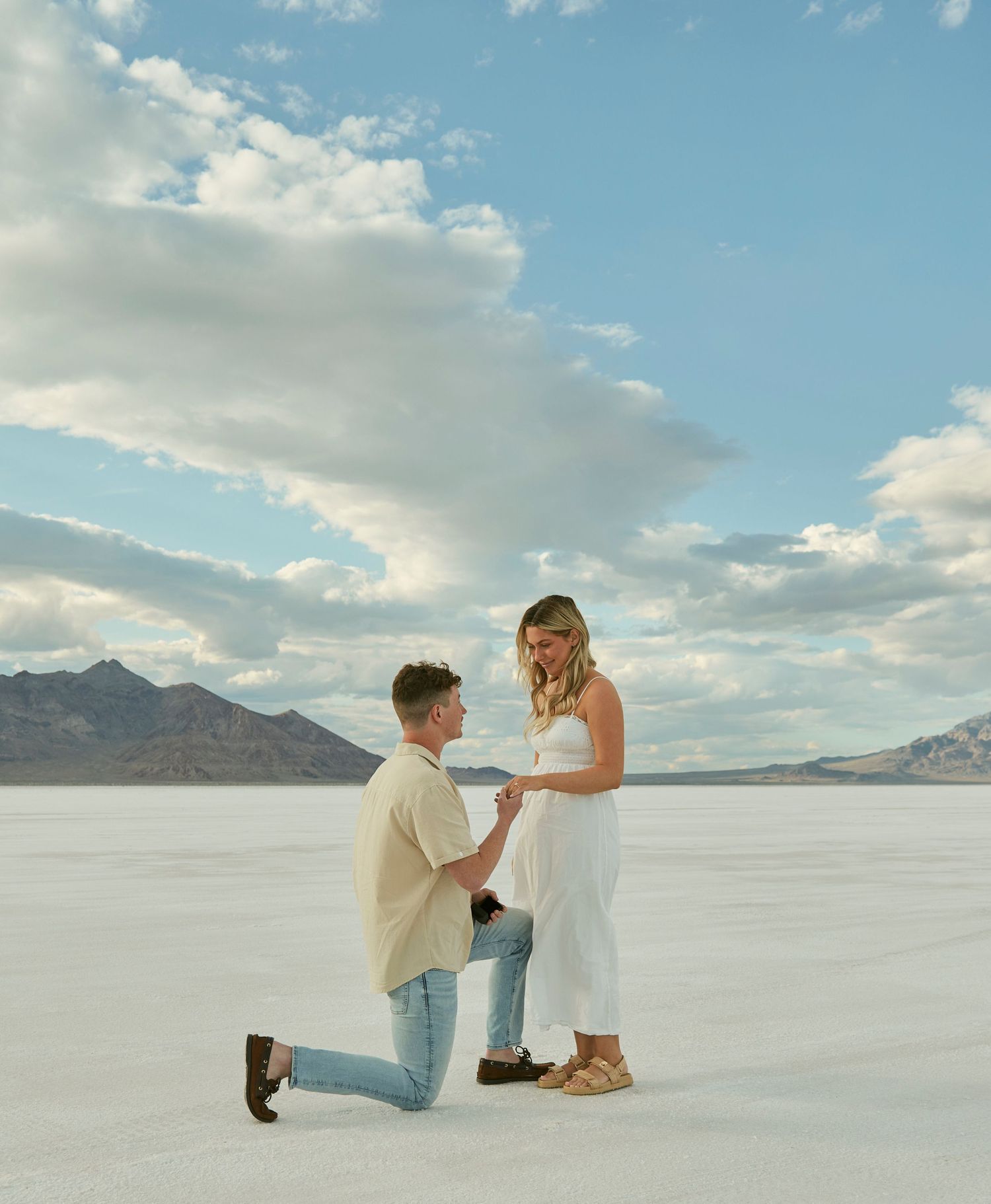 A couple getting engaged on salt flats with dramatic mountain landscape and blue skies.
