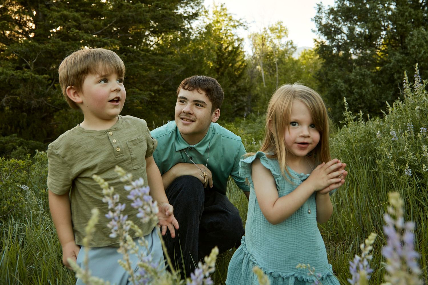 Three children playing outdoors among purple wildflowers in a summer meadow.