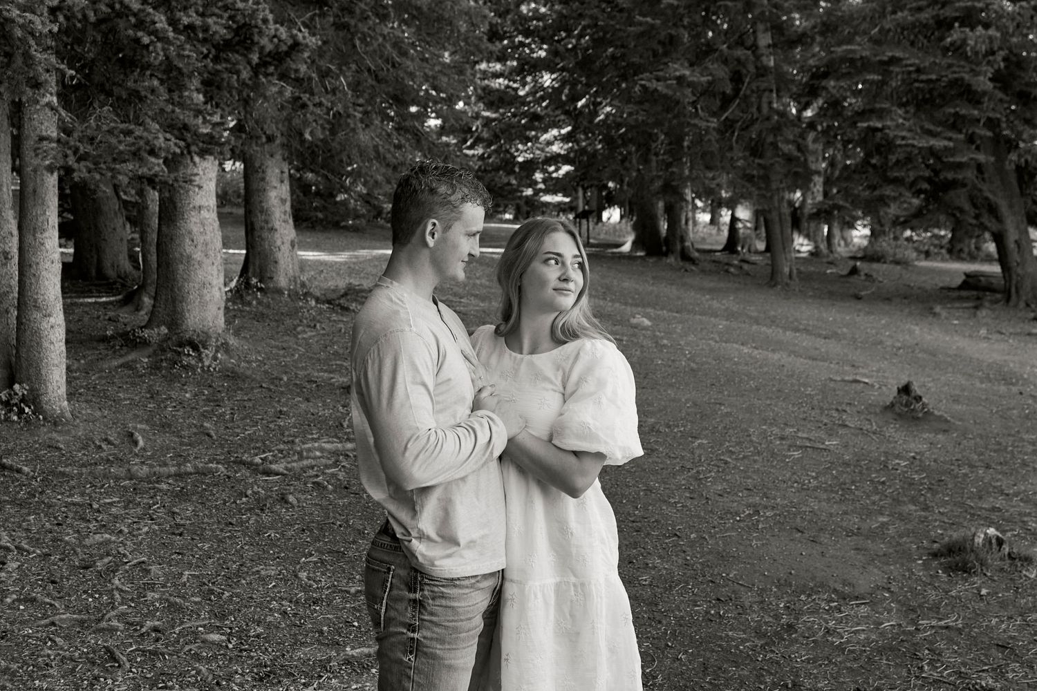 A black and white photograph of a couple sharing a tender moment in a forest setting.