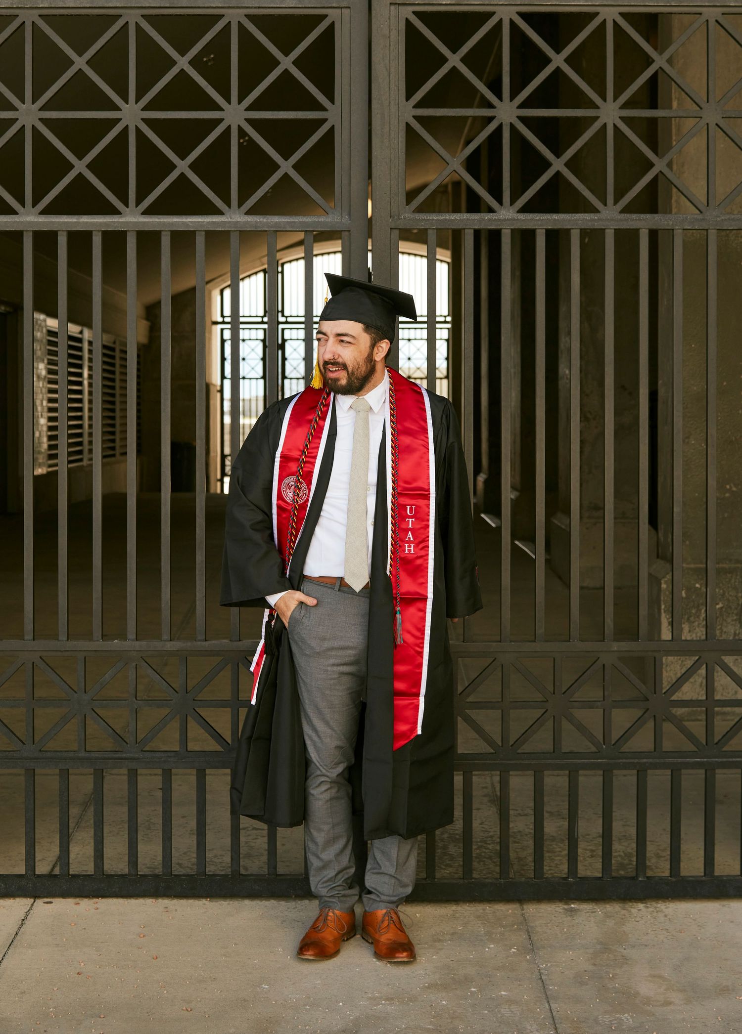 Graduate in cap and gown standing in front of decorative metal gate.