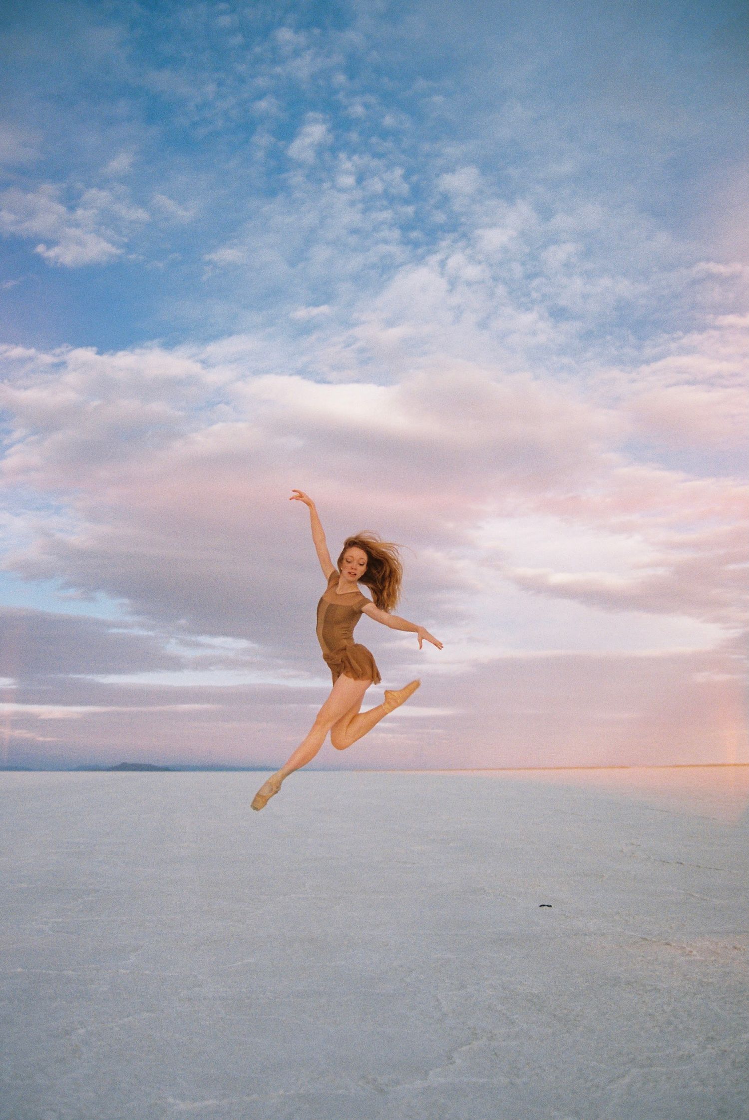 Dynamic dance leap captured against pink sunset sky over salt flats.