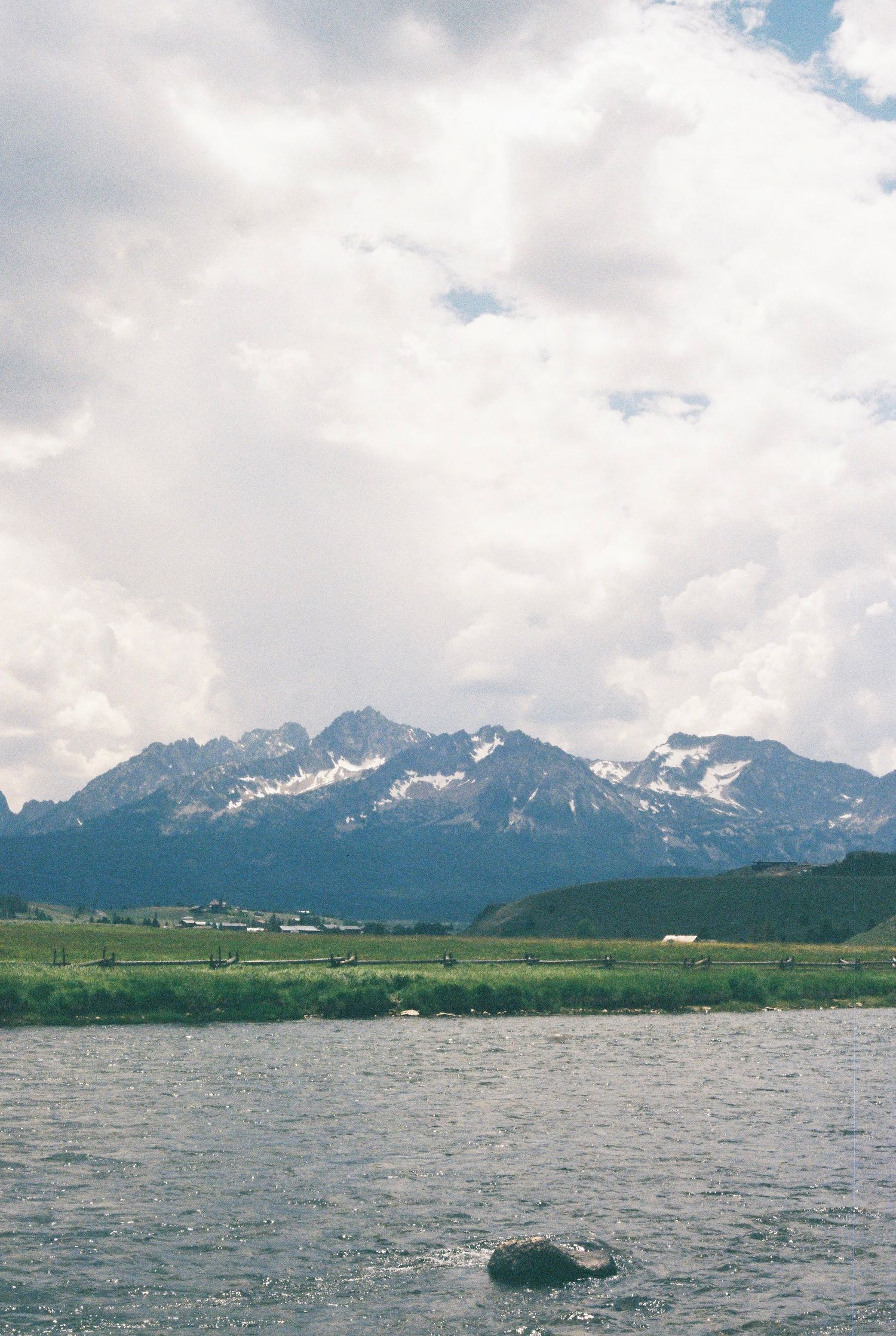 Scenic mountain landscape with snow-capped peaks and a lake in the foreground under cloudy skies.