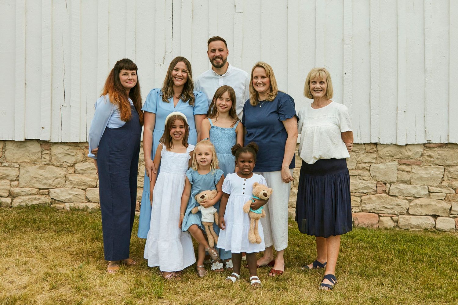Extended family portrait in coordinated blue and white outfits against white barn wall.