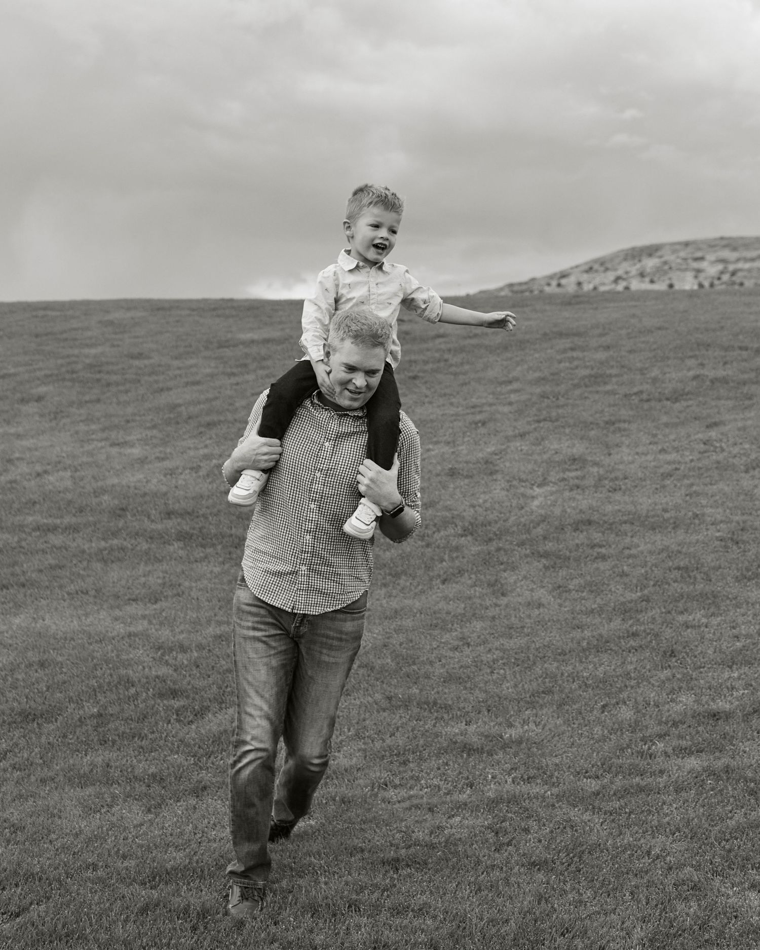 Black and white photo of playful shoulder ride on grassy hillside.