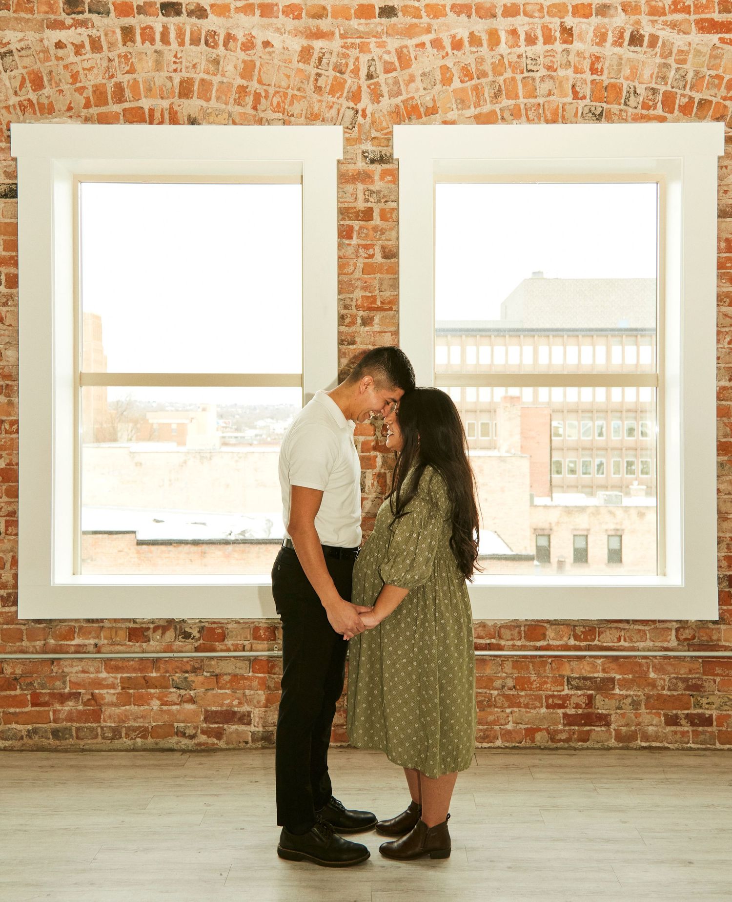 A tender moment shared between a couple by bright windows against exposed brick walls.