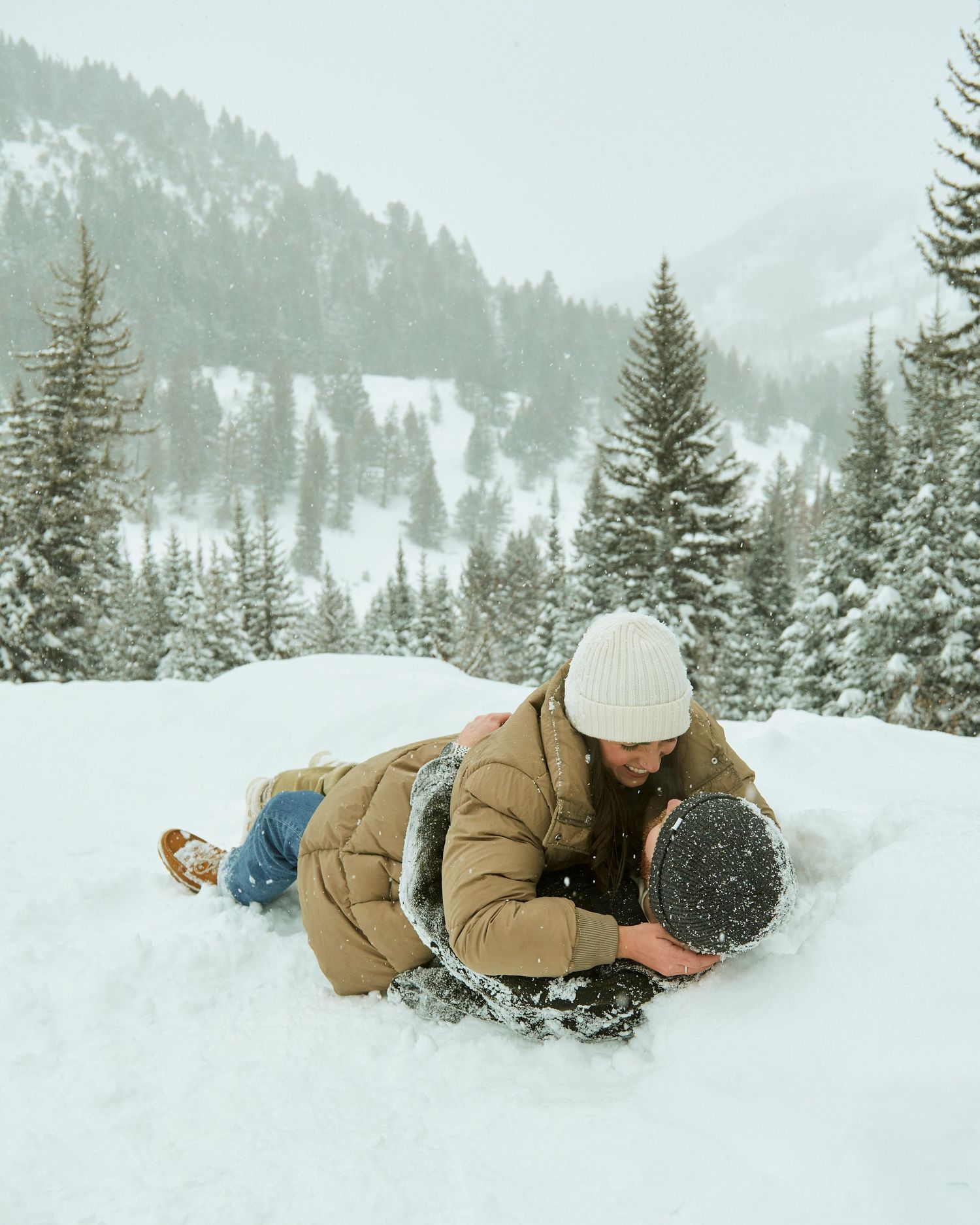 Playful couple lying in snow together during winter photoshoot.