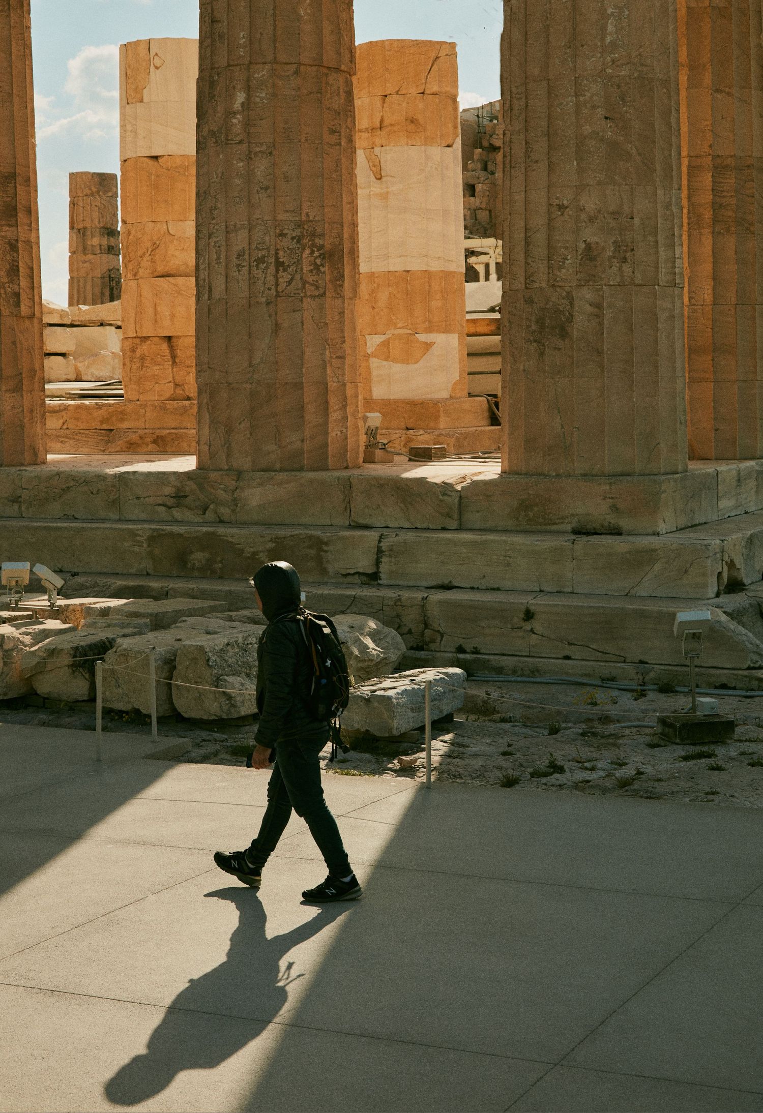 Ancient Greek temple columns casting long shadows with a silhouetted figure walking through.
