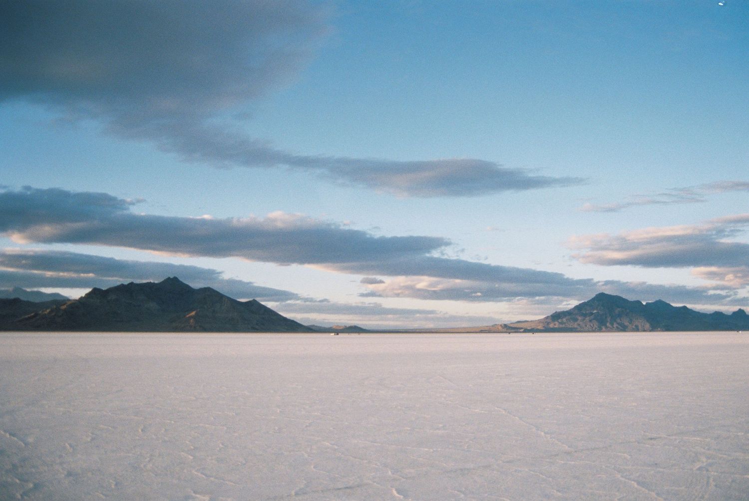 Panoramic view of mountains surrounding the expansive white salt flats under evening clouds.