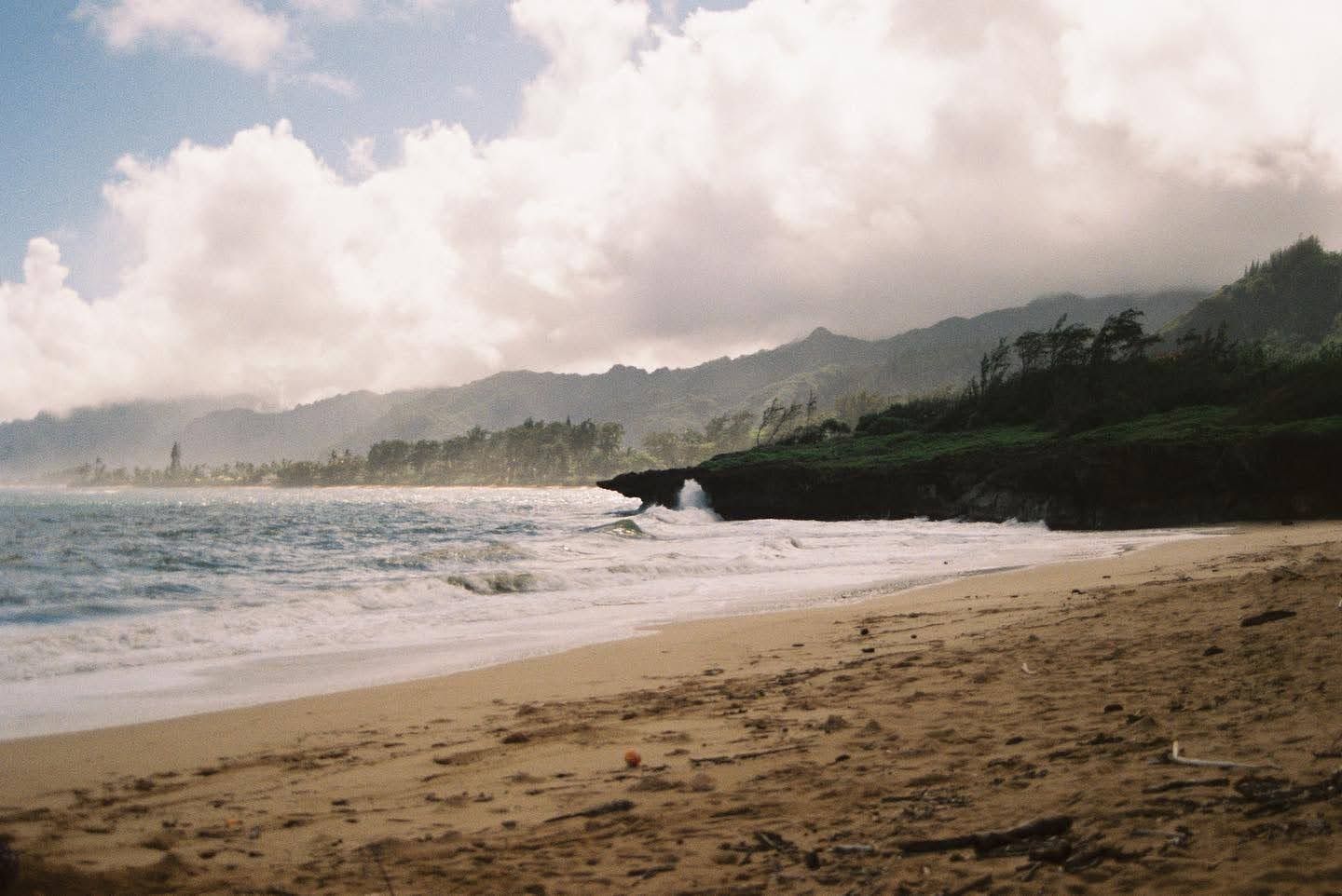 Misty coastal beach landscape with mountains and rocky cliffs along a sandy shoreline.