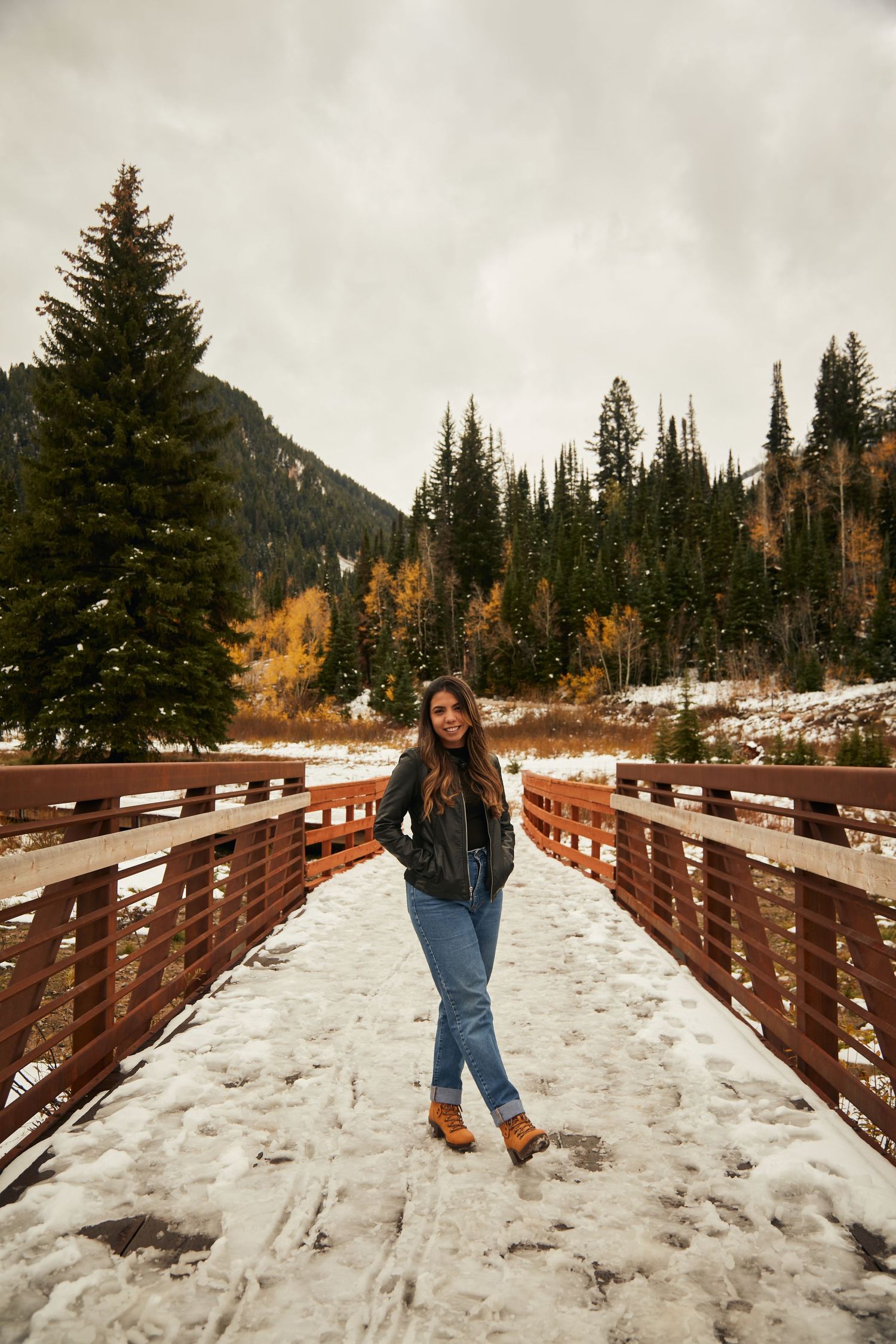 Winter portrait on a snowy wooden bridge with mountain scenery and evergreen trees.
