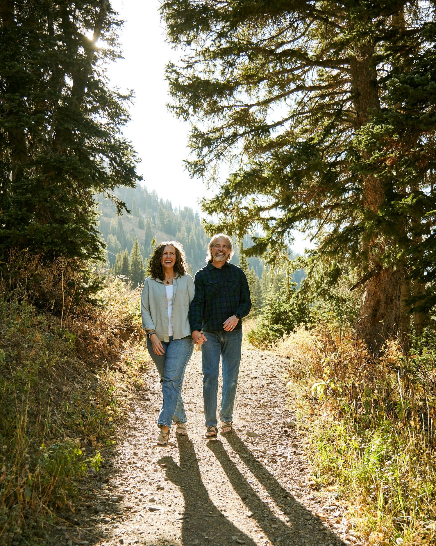 Couple walking together on sunny forest trail casting long shadows.