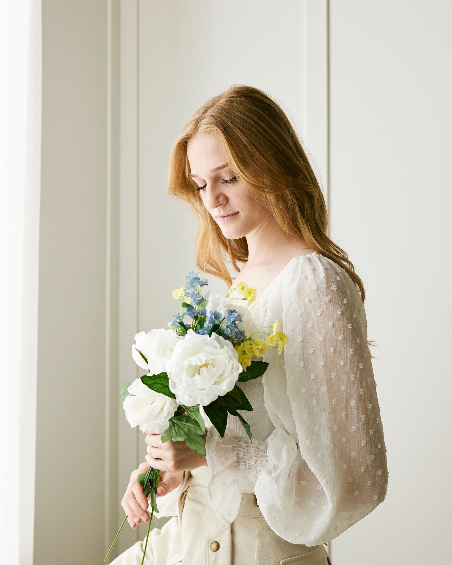 Elegant portrait with white and blue floral bouquet against white wall.
