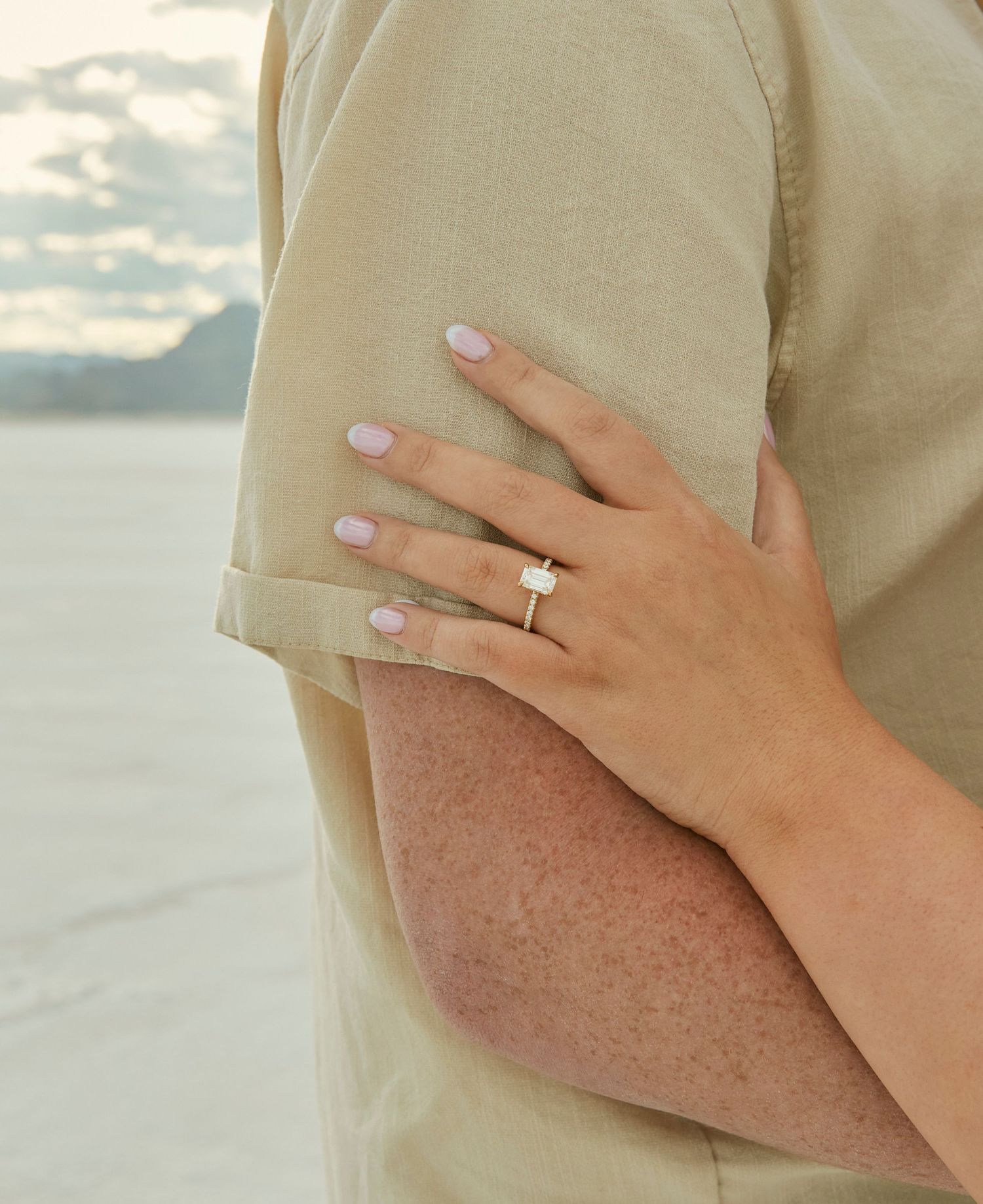A close-up of a hand wearing new engagement ring against beige clothing with salt flats background.