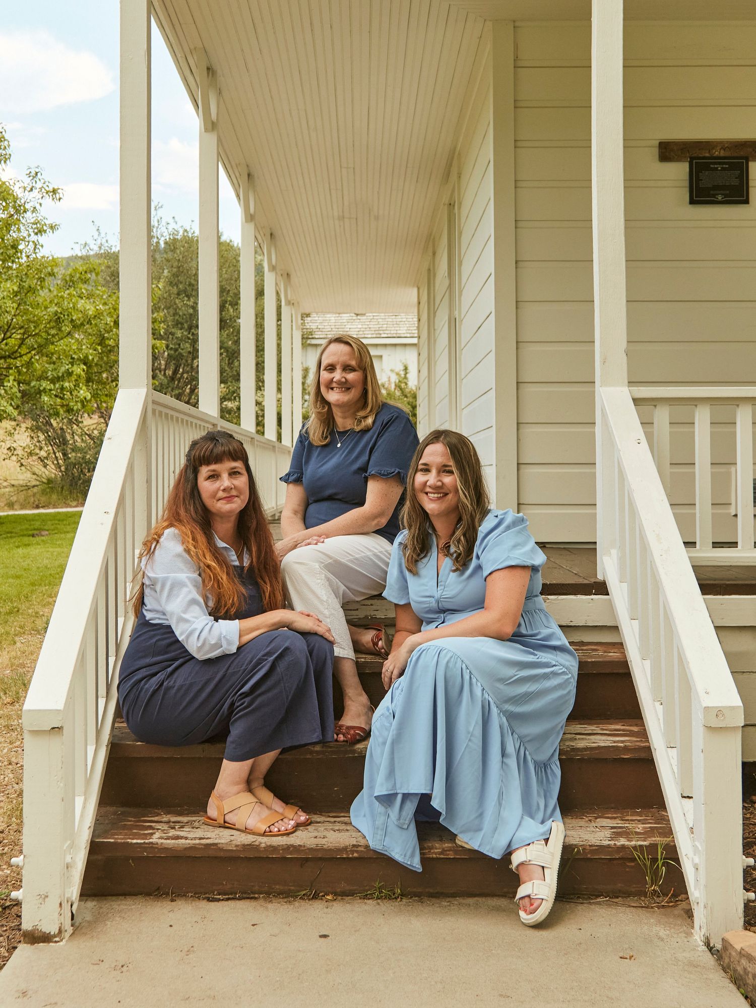 Three people sitting casually on white porch steps wearing coordinated blue outfits.