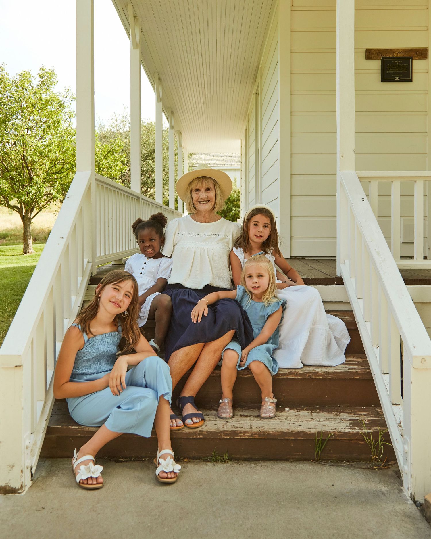 A group sitting together on white farmhouse porch steps wearing coordinated blue and white outfits.