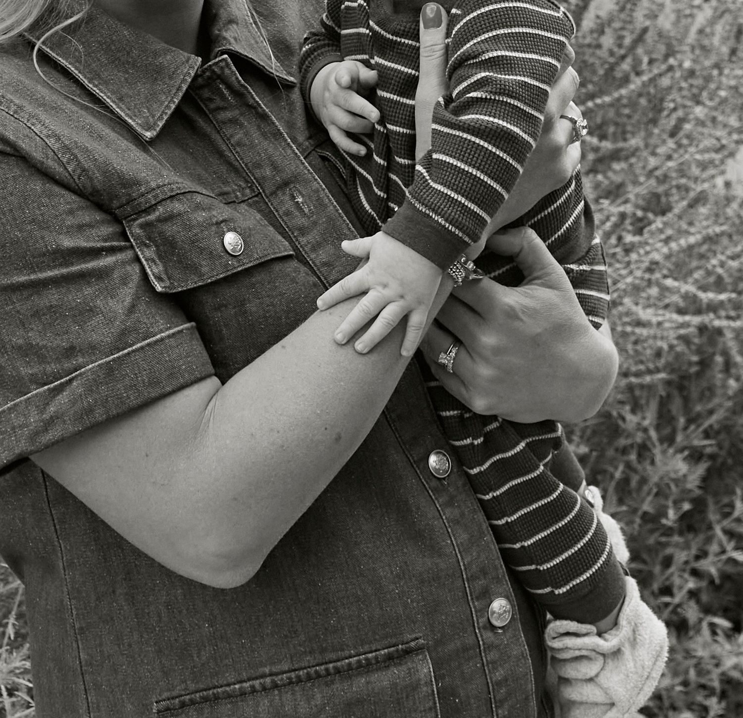 Close up black and white image showing arms holding a baby wearing a striped shirt.